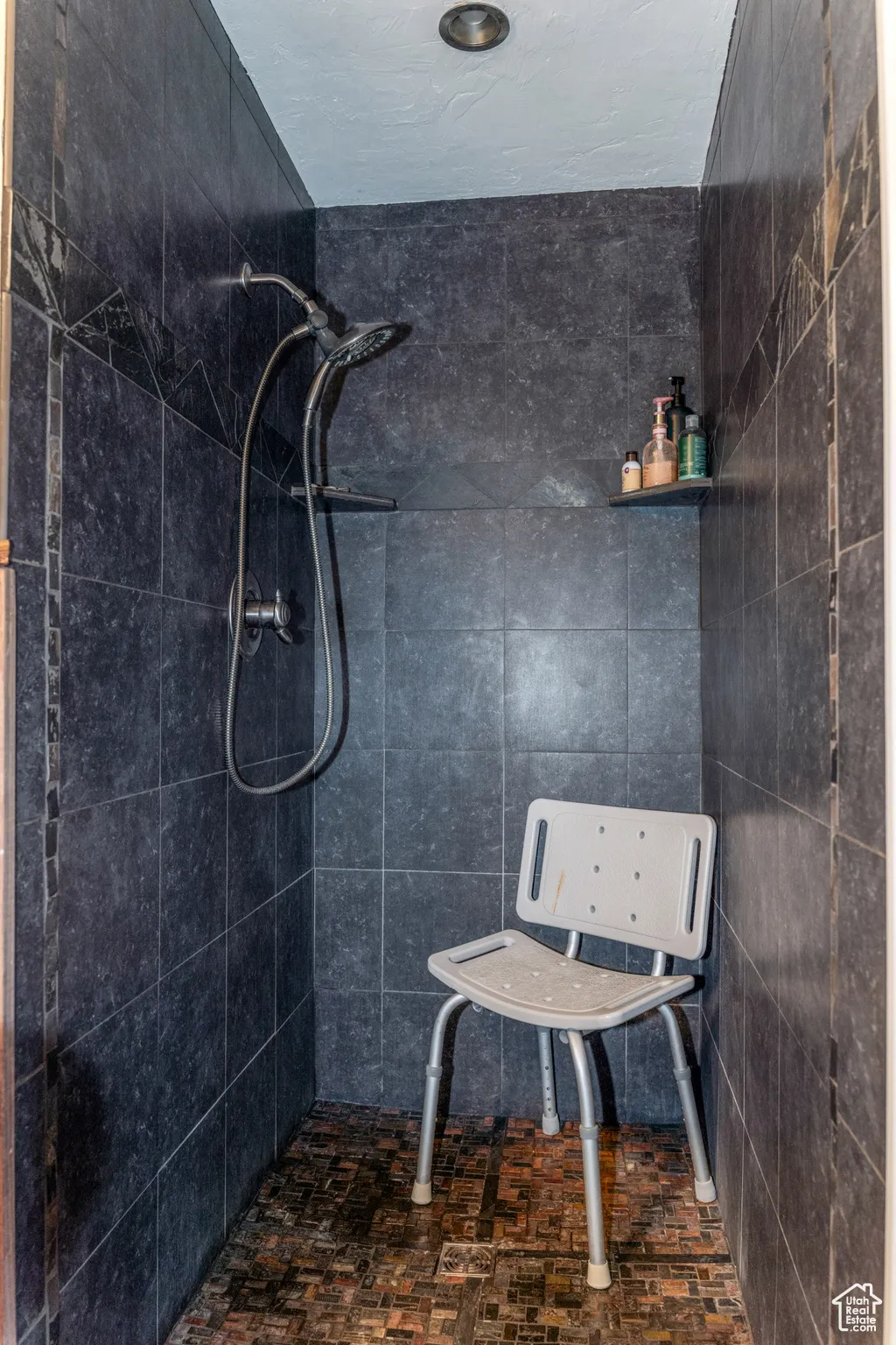 Walk-in shower featuring dark tile walls with an accent border, a mosaic tile floor, and a built-in shower niche