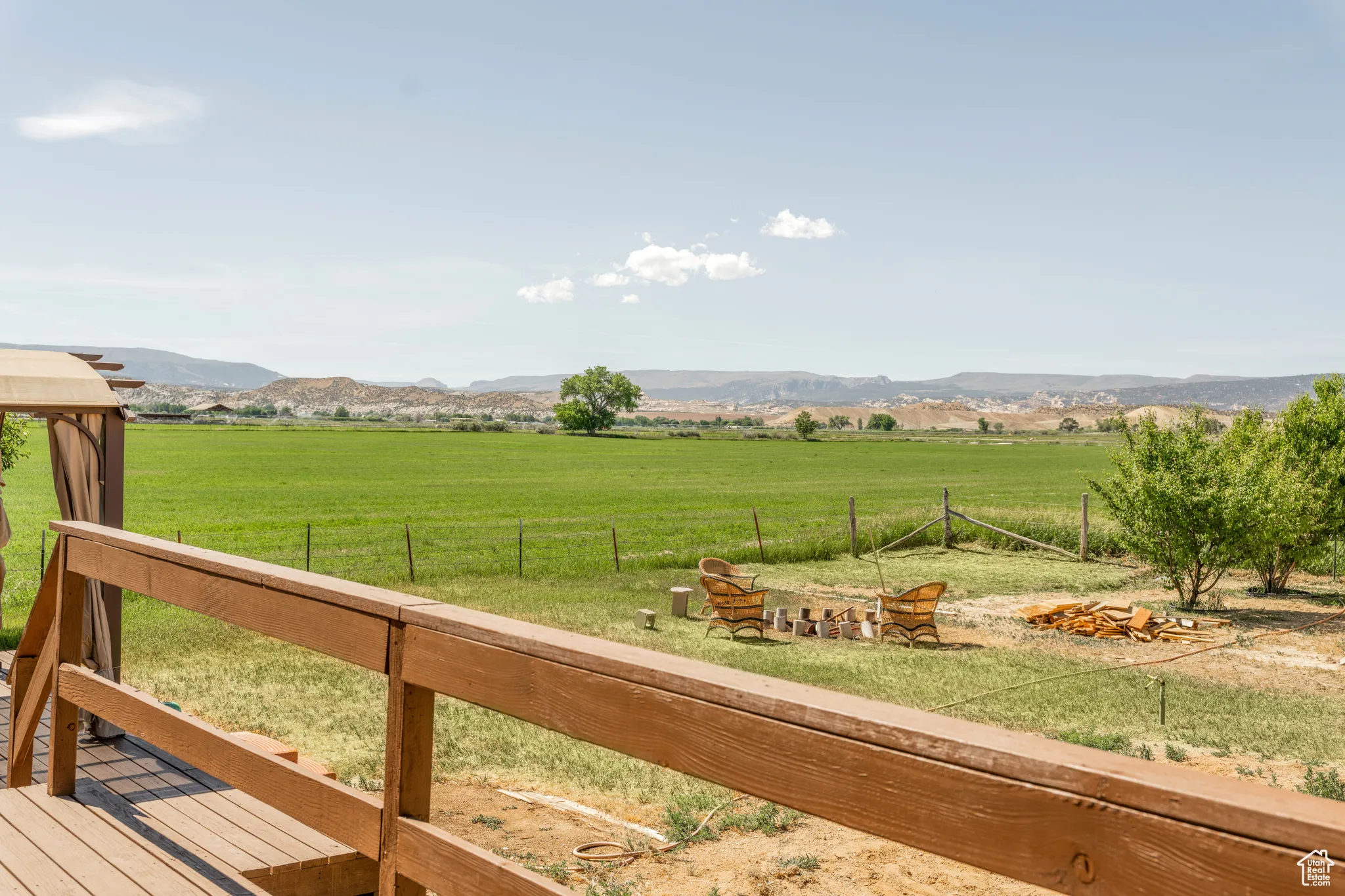 Expansive green field with distant hills, bordered by a wooden fence and mature trees