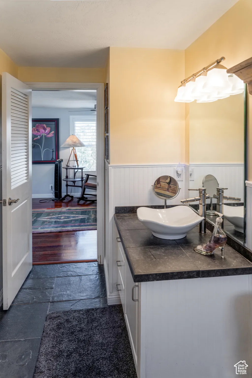 Bathroom vanity with a white vessel sink, dark countertop, and white beadboard cabinetry