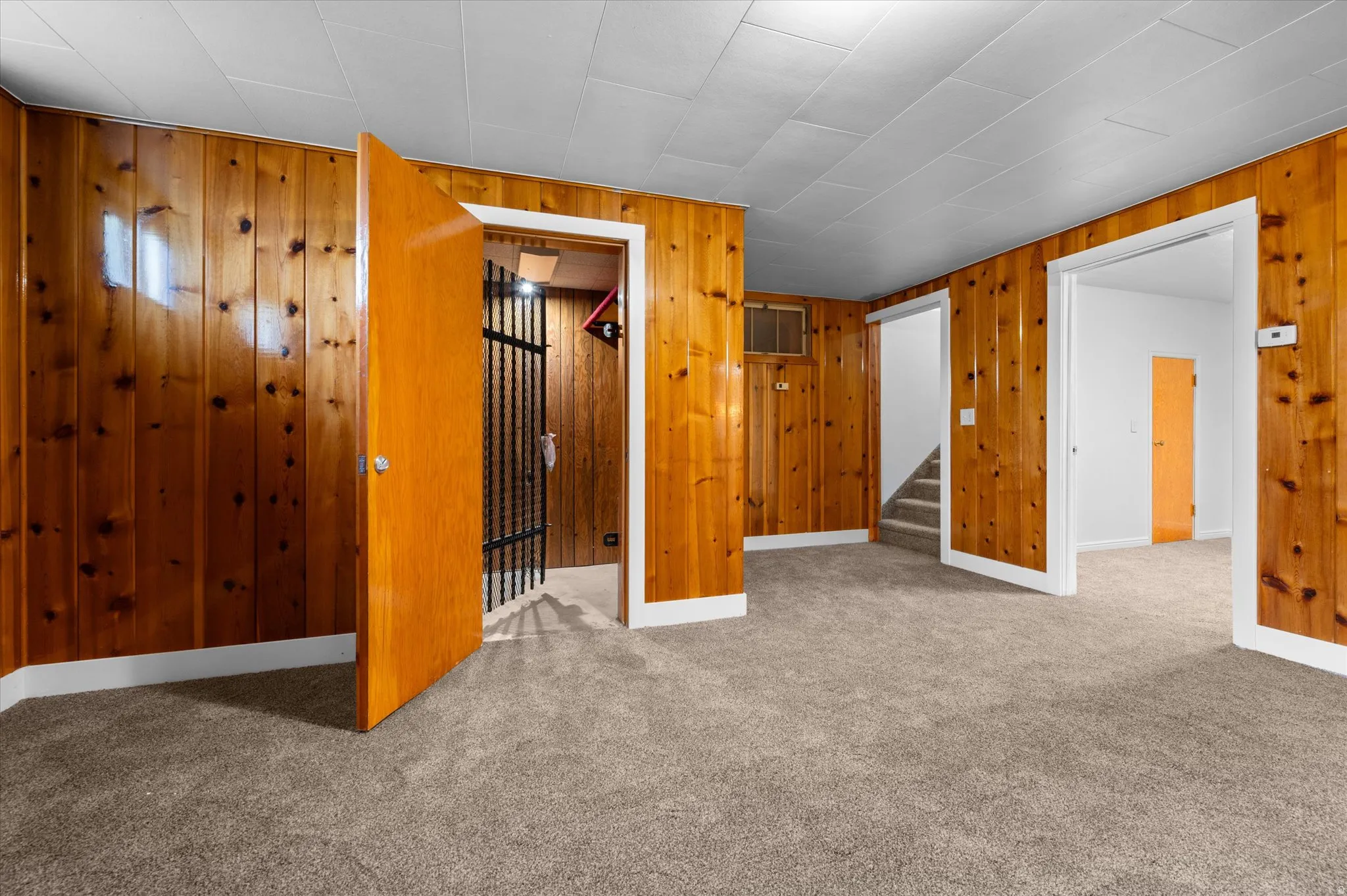 Spacious room featuring wood-paneled walls and neutral carpeting