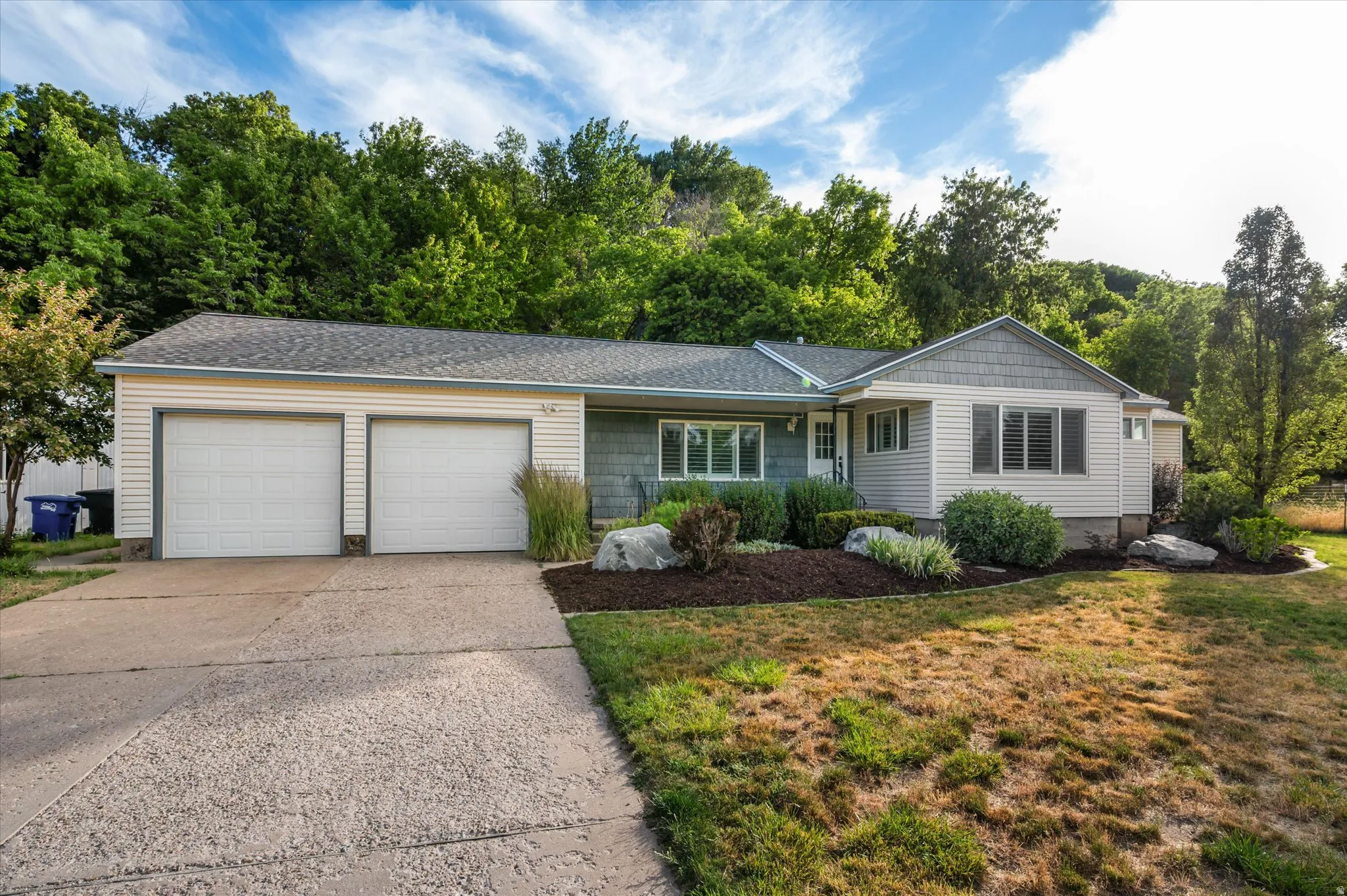 Ranch-style residence featuring a two-car garage with white paneled doors, partial horizontal siding and shake siding, and a gabled roofline