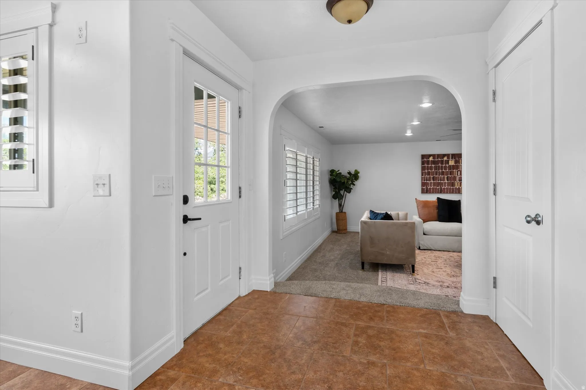 Foyer with tile flooring, a white glass-paneled entry door, and a white plantation-shuttered window