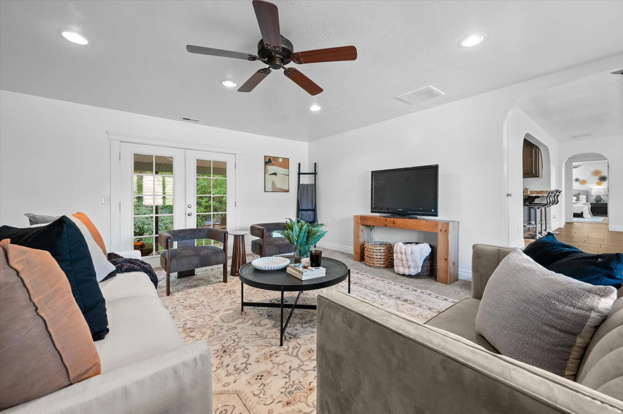 Living area featuring a ceiling fan with integrated lighting, recessed ceiling lights, and double glass-paneled doors