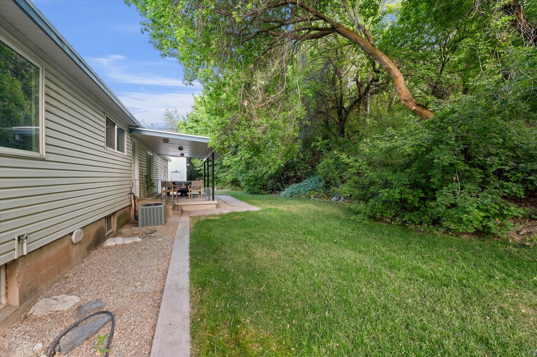 Expansive green lawn with a covered patio, featuring a gravel perimeter and dense mature trees providing a natural backdrop