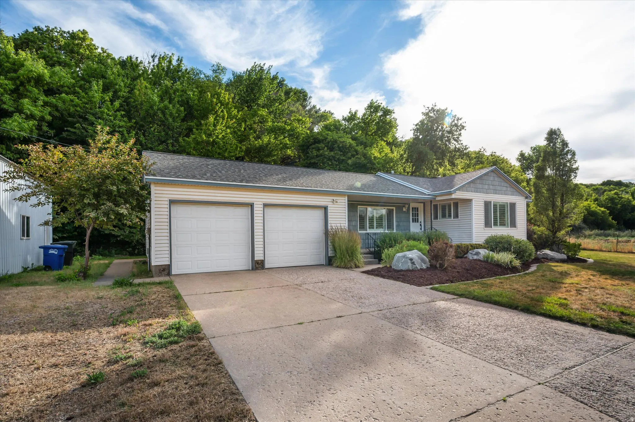 Ranch-style residence featuring a two-car garage with white paneled doors, light-colored siding, and a gabled roofline