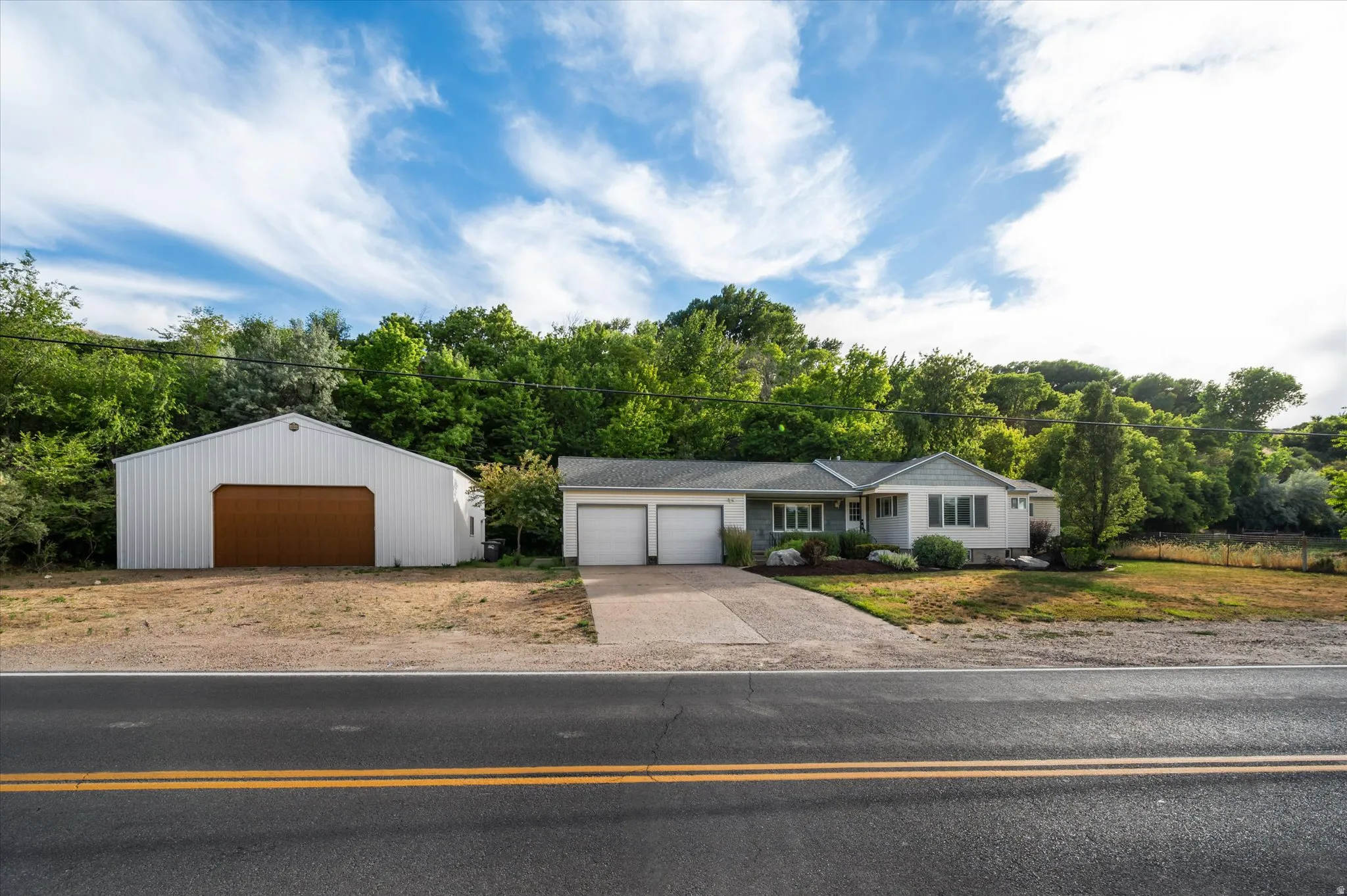 Ranch-style residence featuring a two-car garage, established front landscaping, and a separate large outbuilding with an overhead door