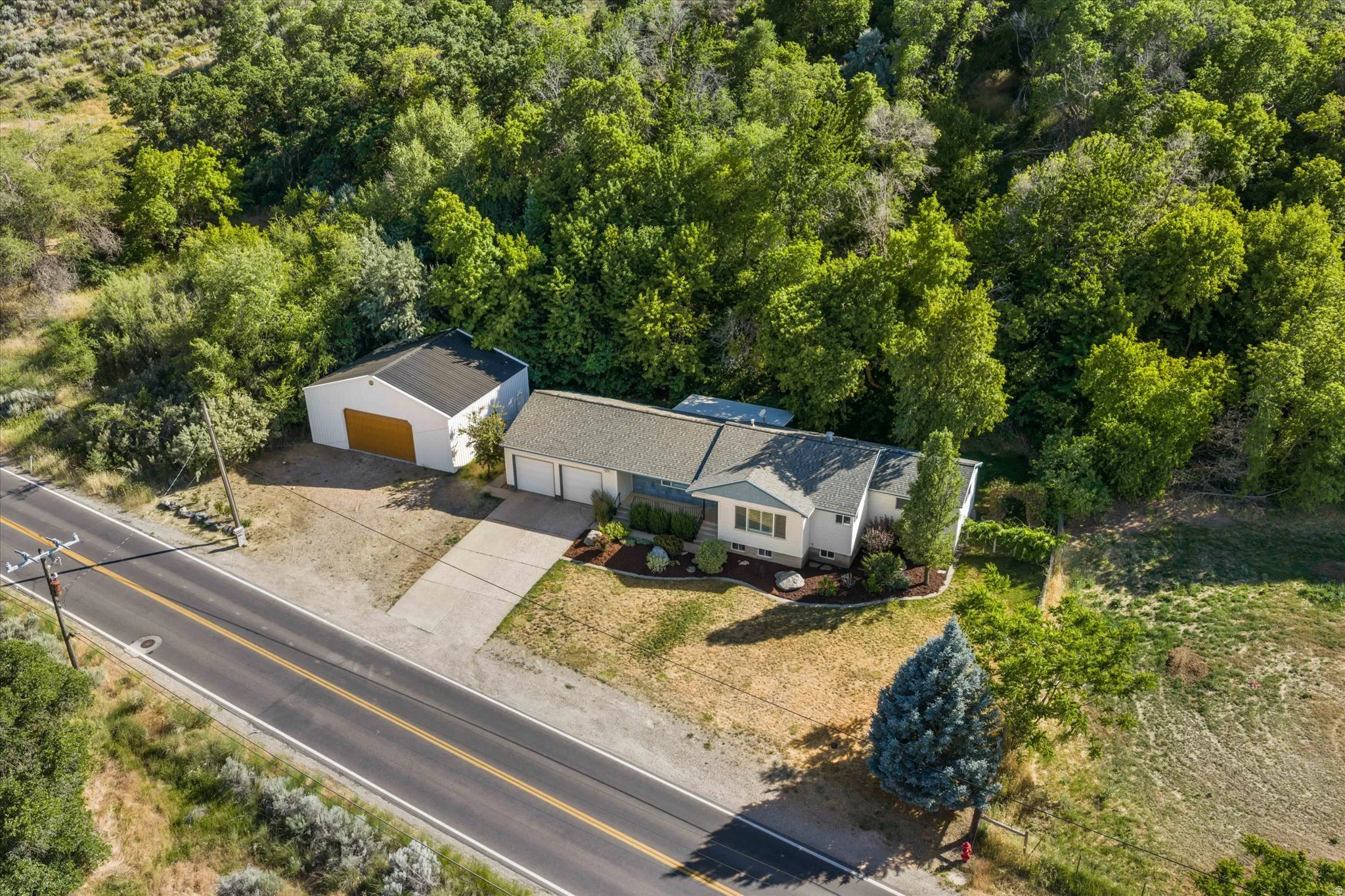 Property featuring a main residence with a two-car garage, a detached white outbuilding with a single garage door, a concrete driveway, and mature landscaping