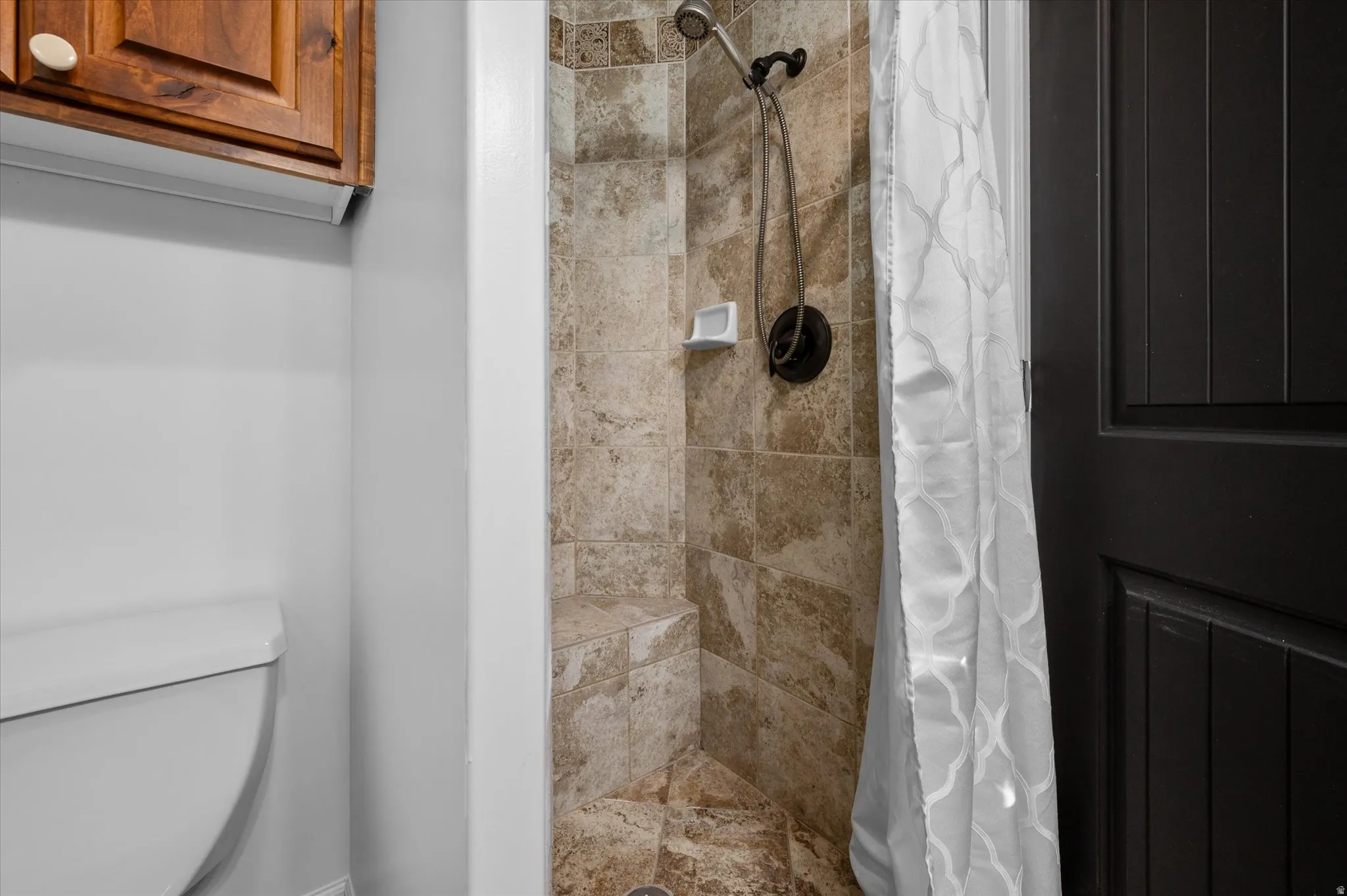 Tiled shower with a built-in bench, dark bronze fixtures, and a handheld showerhead