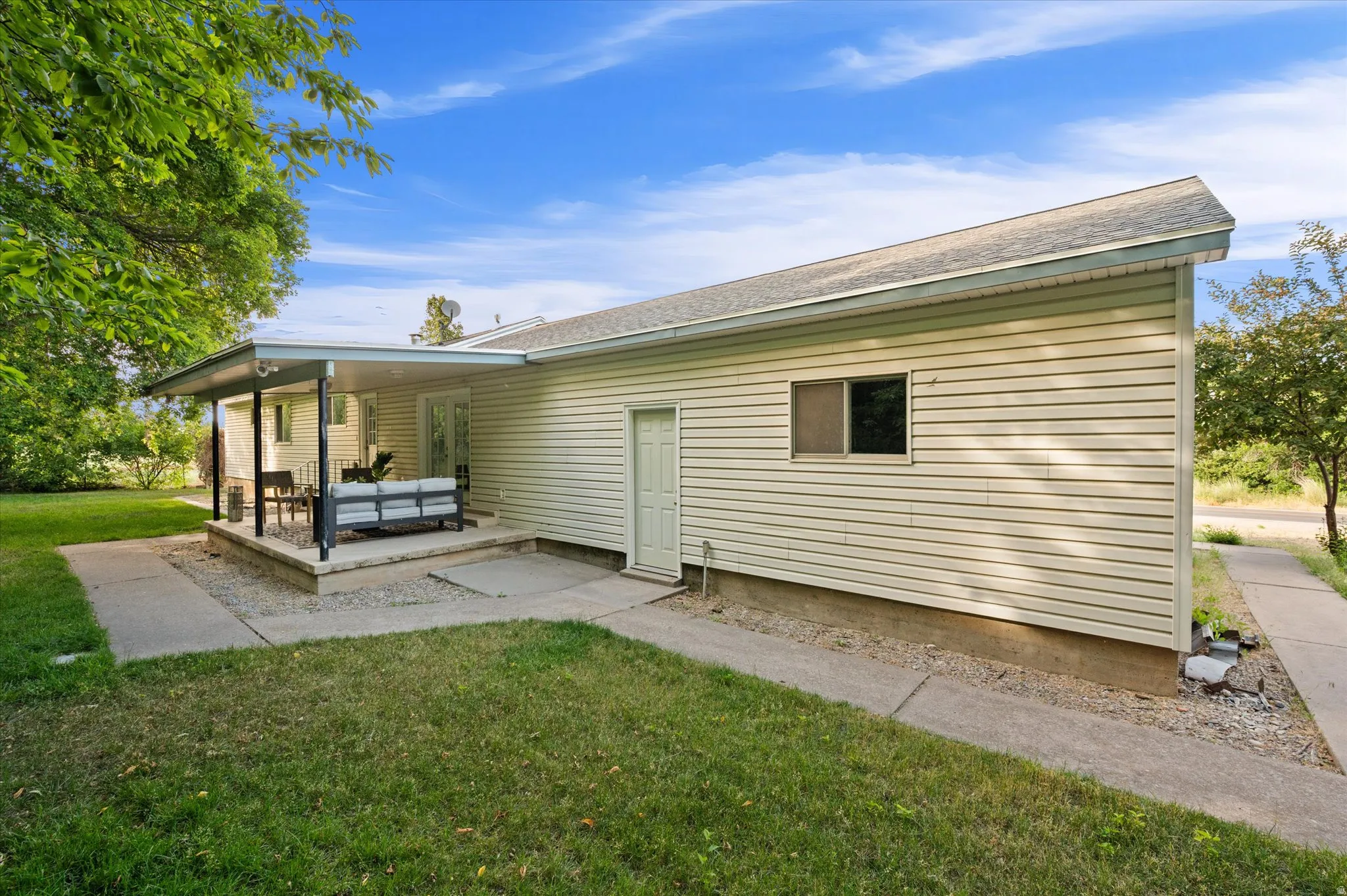 Side exterior featuring vinyl siding, a covered patio, concrete walkways, a side entry door, and a single window