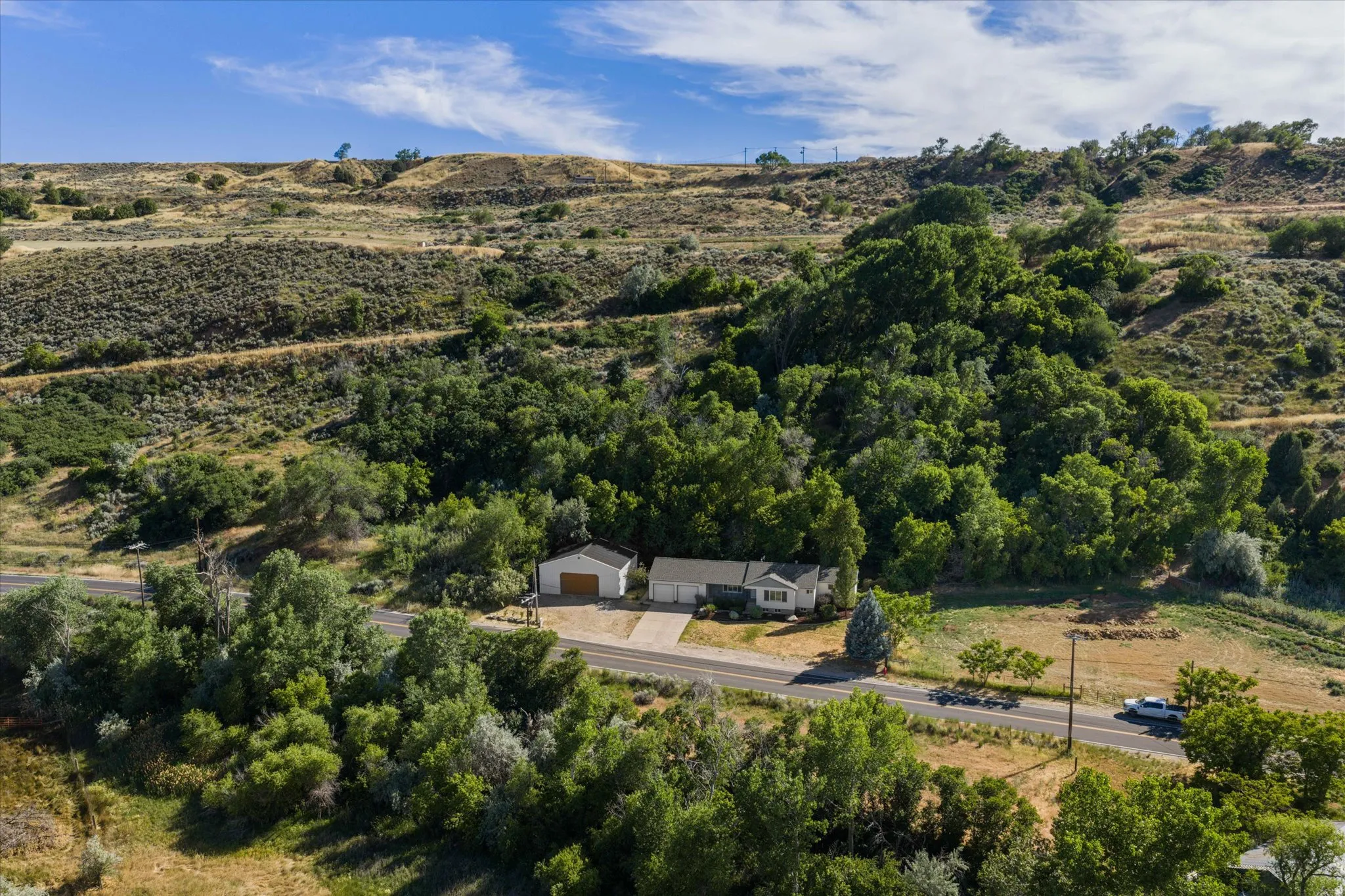Ranch-style residence featuring a detached garage, expansive paved driveway, and lush surrounding trees