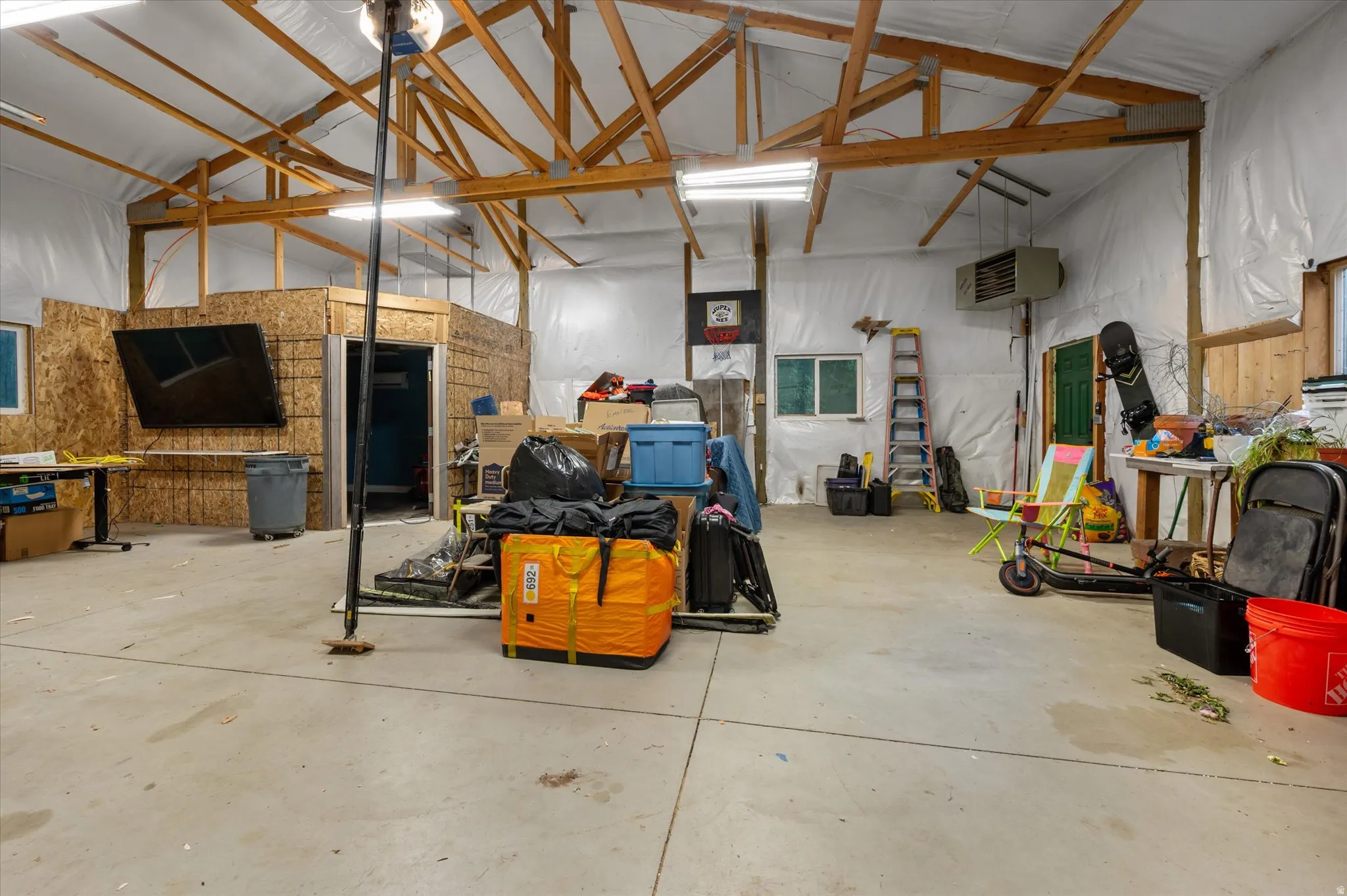 Spacious utility room featuring a concrete floor, exposed wood ceiling trusses, and white wall insulation