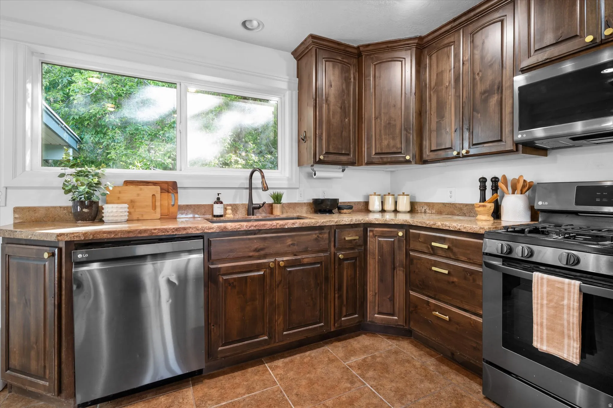 Kitchen featuring rich wood cabinetry with gold-tone hardware, granite-style countertops, and a full suite of stainless steel appliances including a built-in microwave and gas range