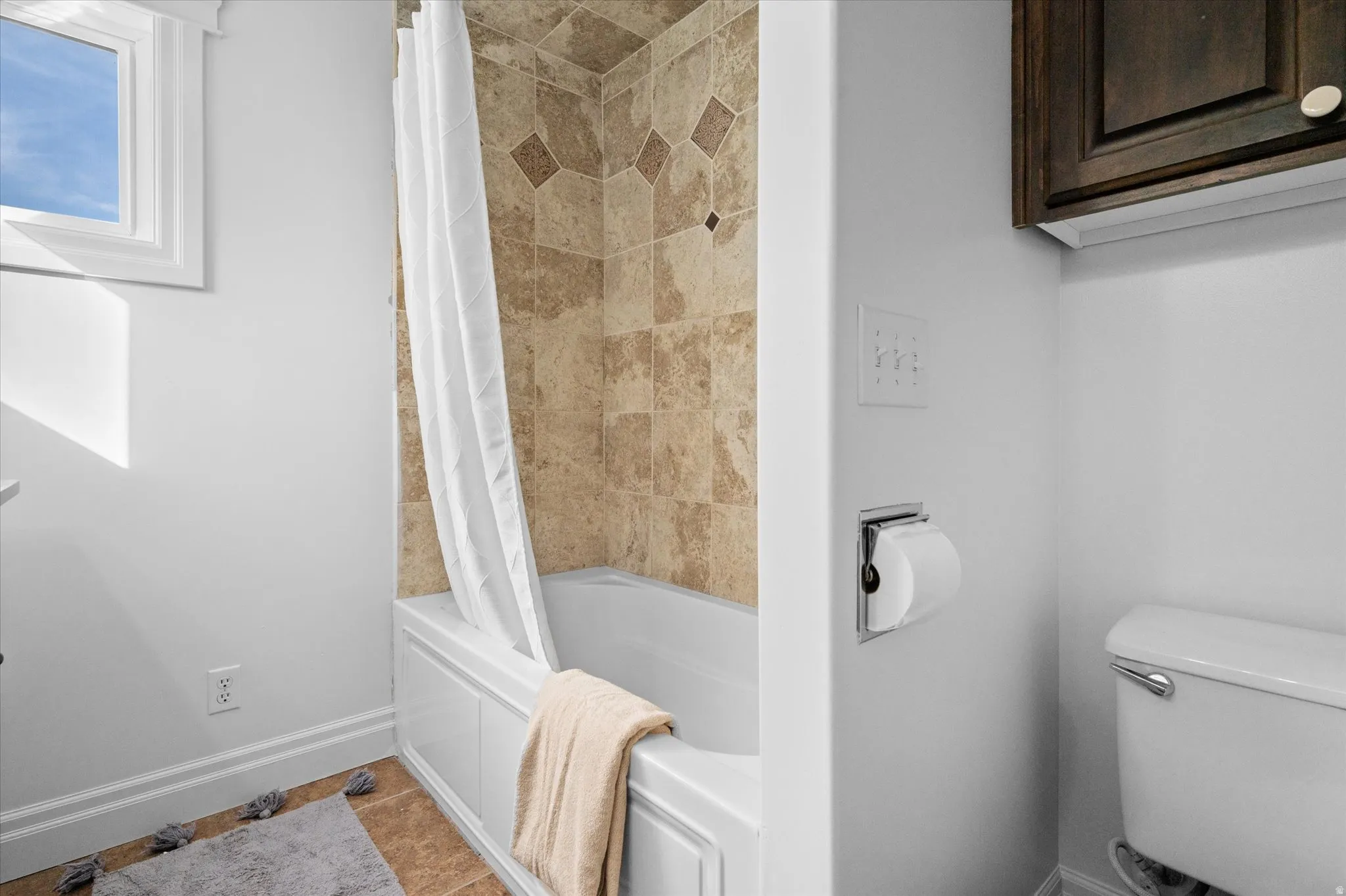 Bathroom featuring a white bathtub with a tiled surround, a window, a toilet, and dark wood cabinetry