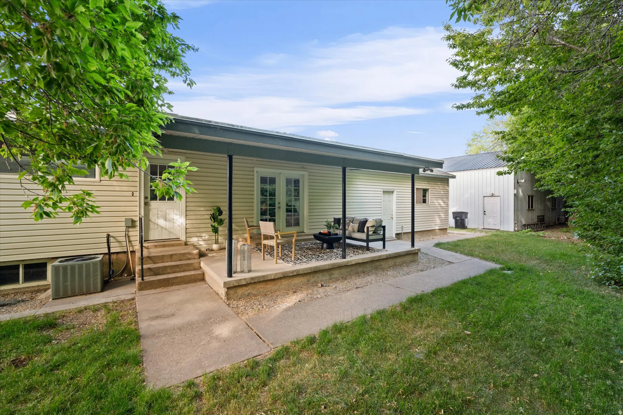 Covered patio with concrete flooring, supported by dark posts, featuring direct access via French doors