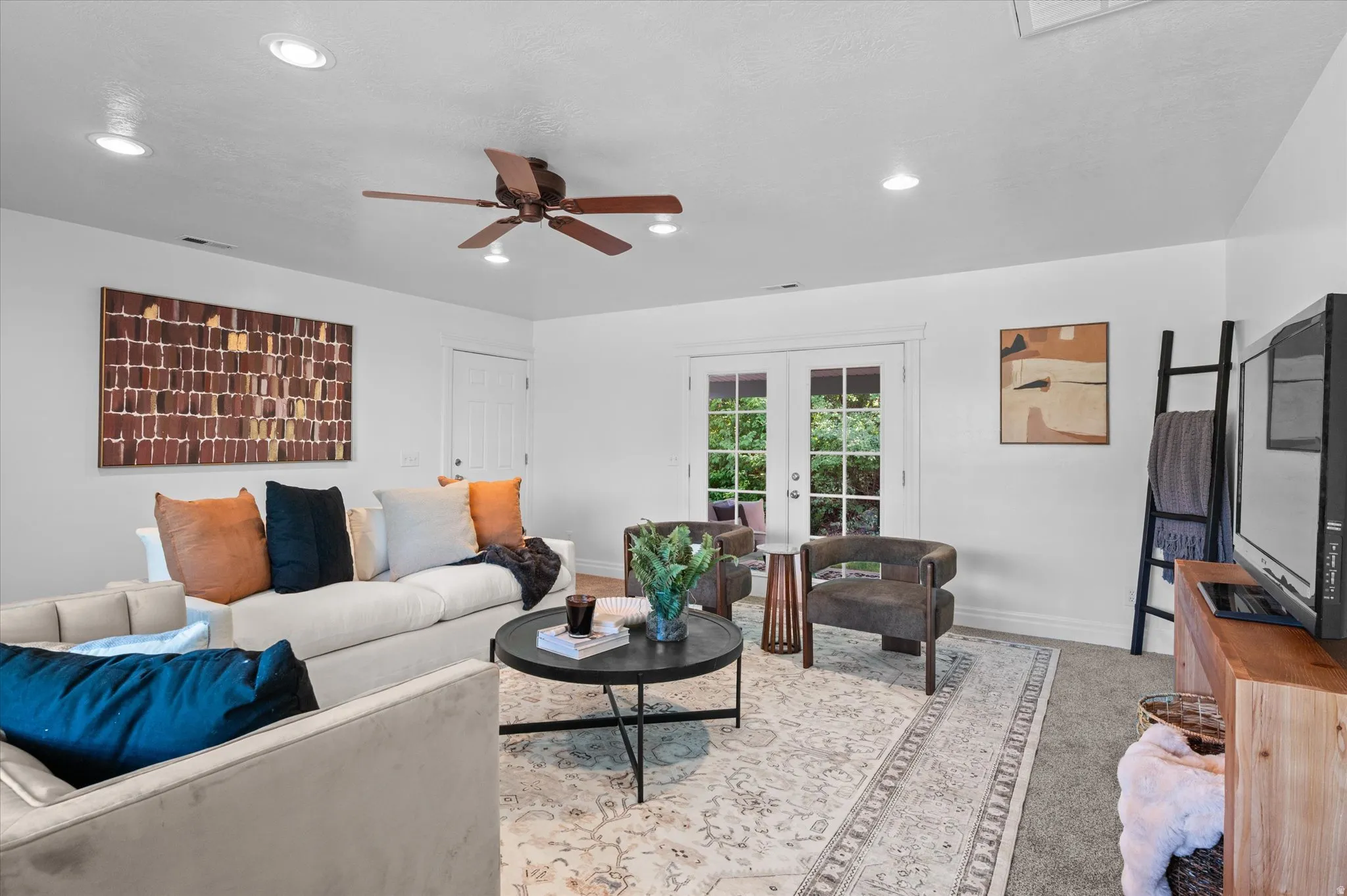 Recessed lighting illuminates this bright living space featuring a ceiling fan, light-toned walls, and a combination of carpet and an area rug