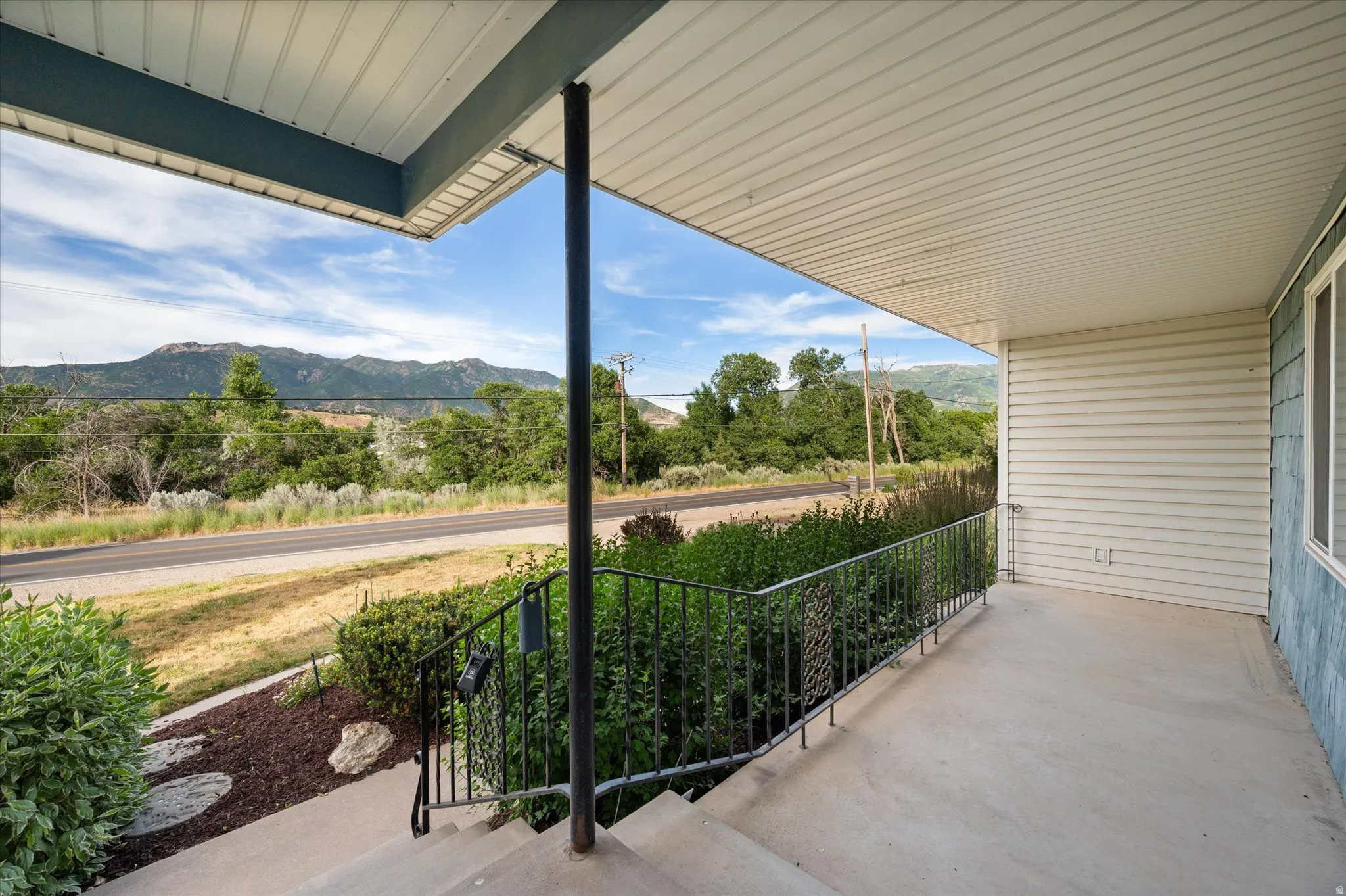 Covered front porch featuring a concrete surface, black metal railing, and white vinyl siding
