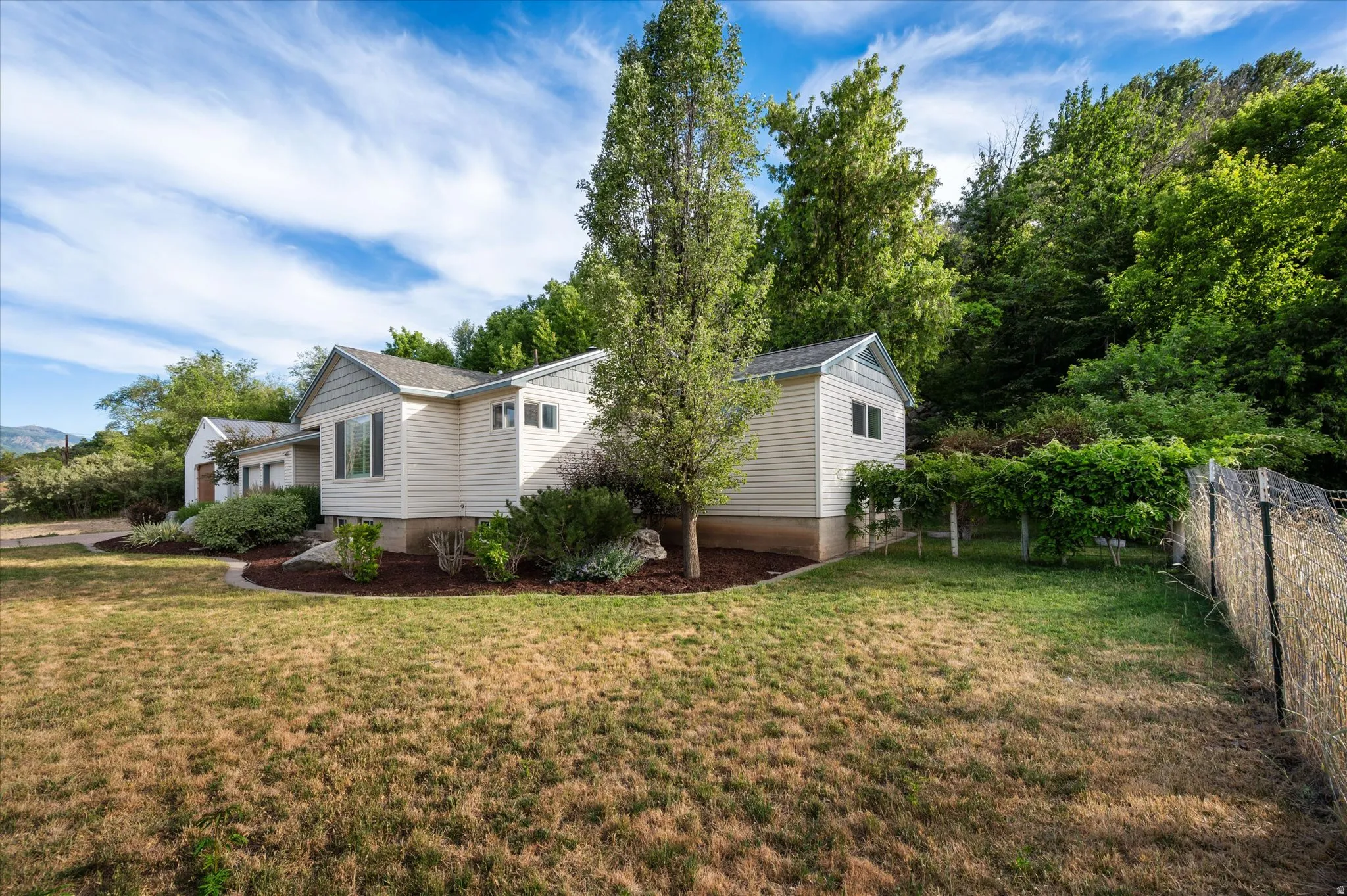 Single-story siding residence featuring a gabled roofline, mature trees, and established landscaping