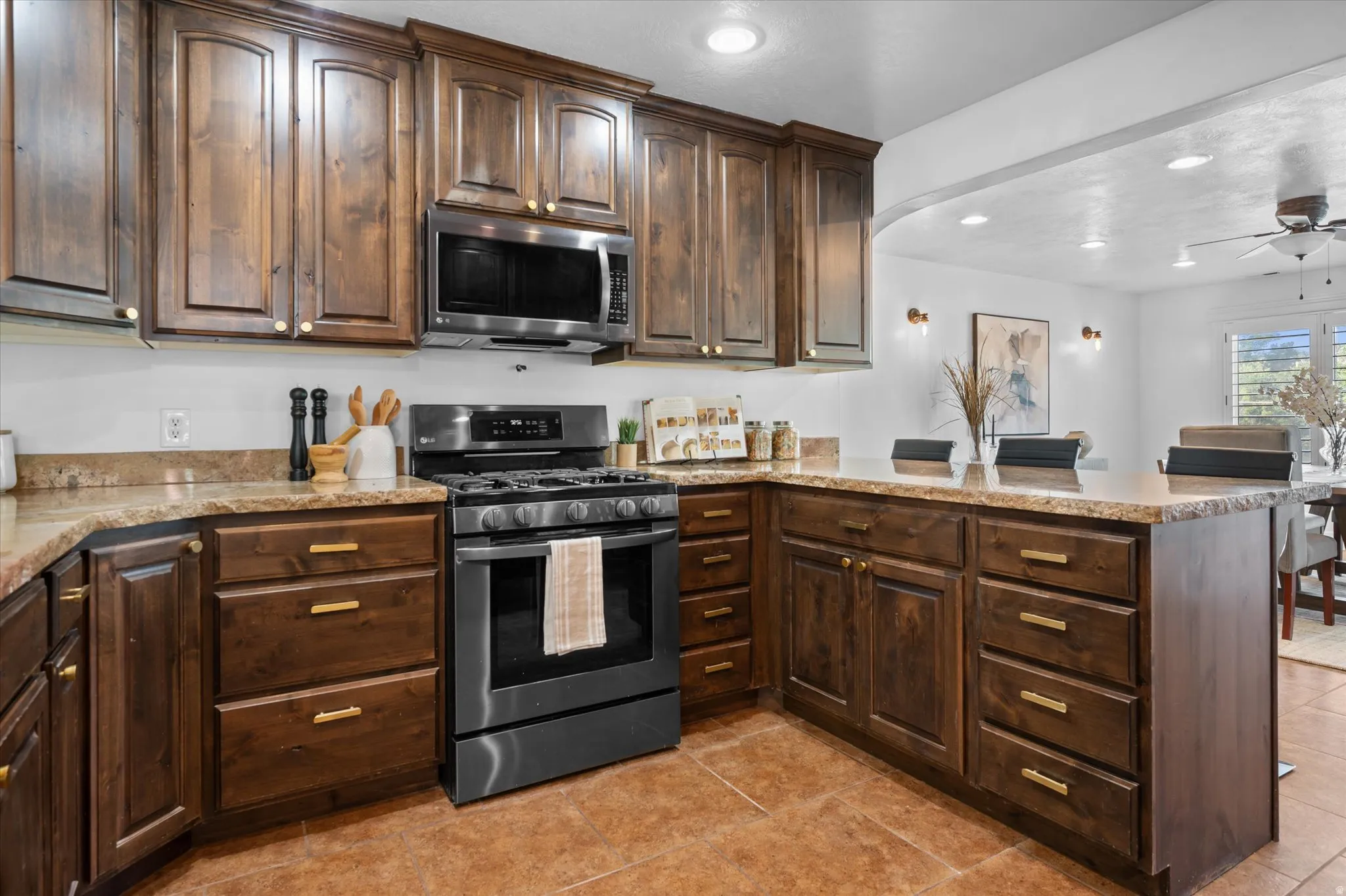 Kitchen featuring rich wood cabinetry with brass hardware, speckled countertops, and a black stainless steel range with an overhead microwave