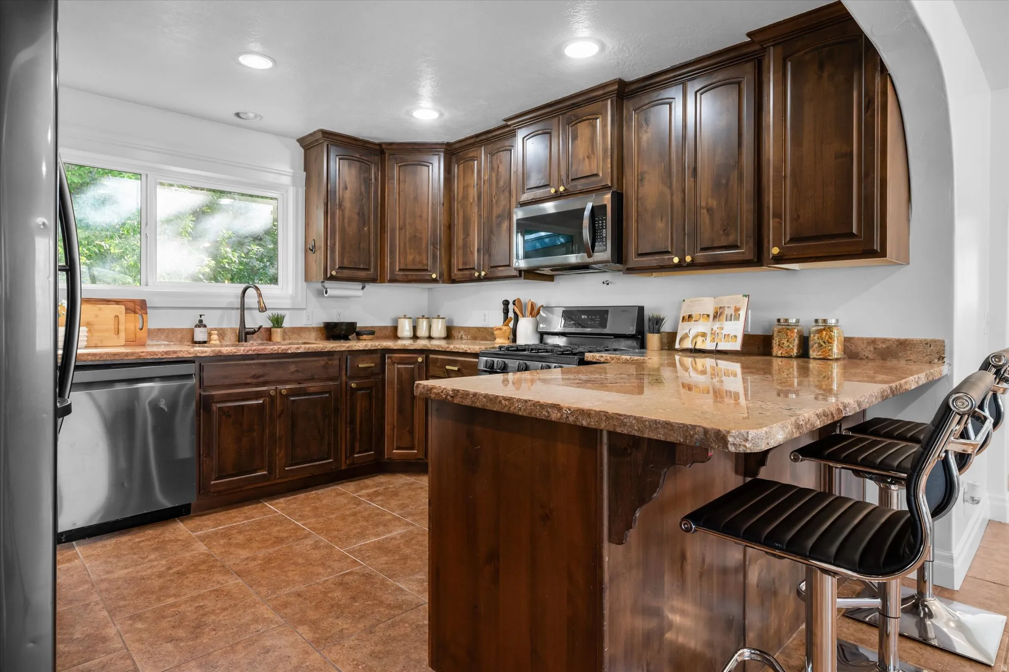 Kitchen featuring rich wood cabinetry, granite countertops, stainless steel appliances, recessed lighting, and tile flooring