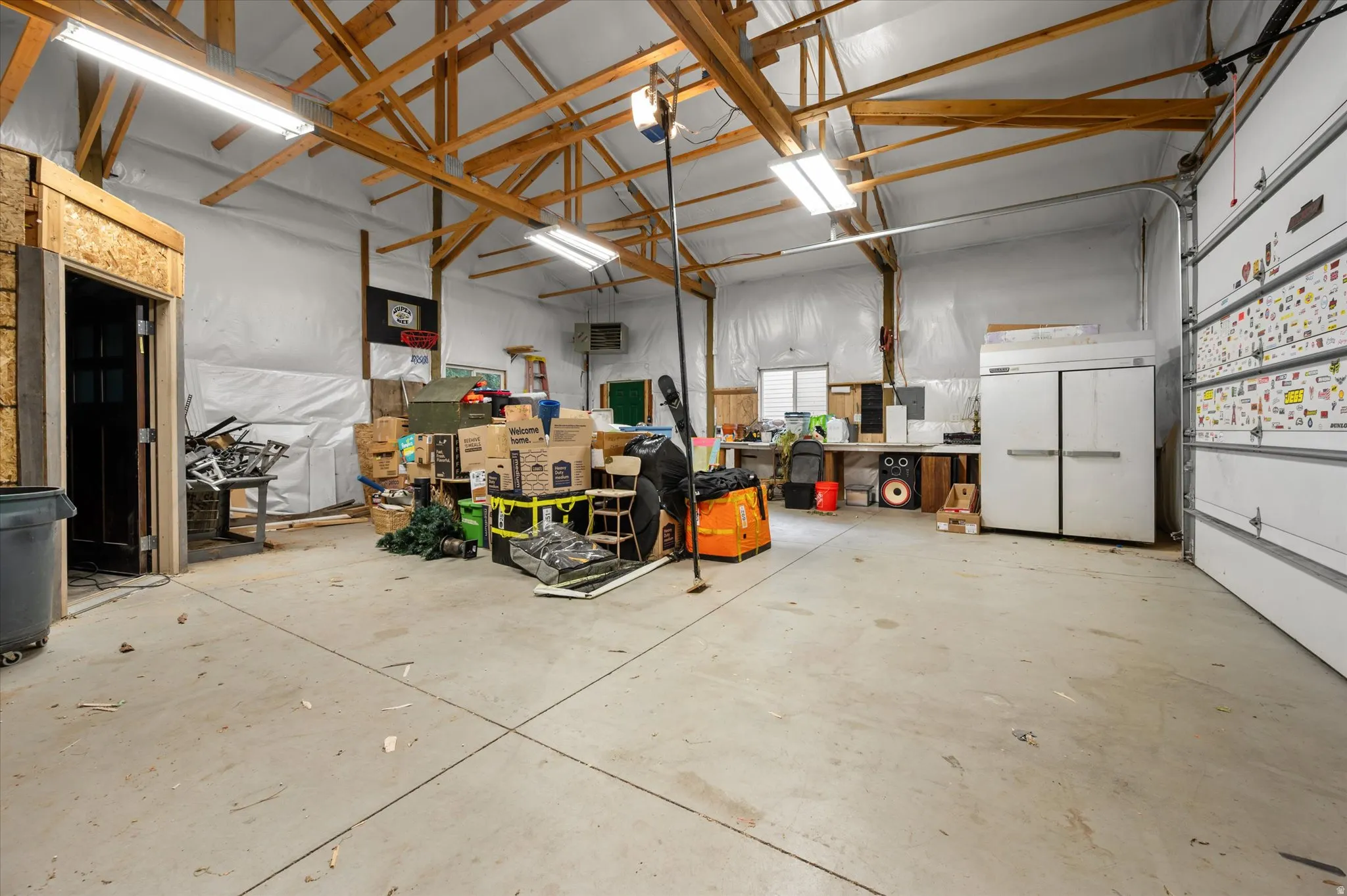 Spacious garage featuring exposed wood beam ceilings, multiple fluorescent lighting fixtures, and a concrete floor