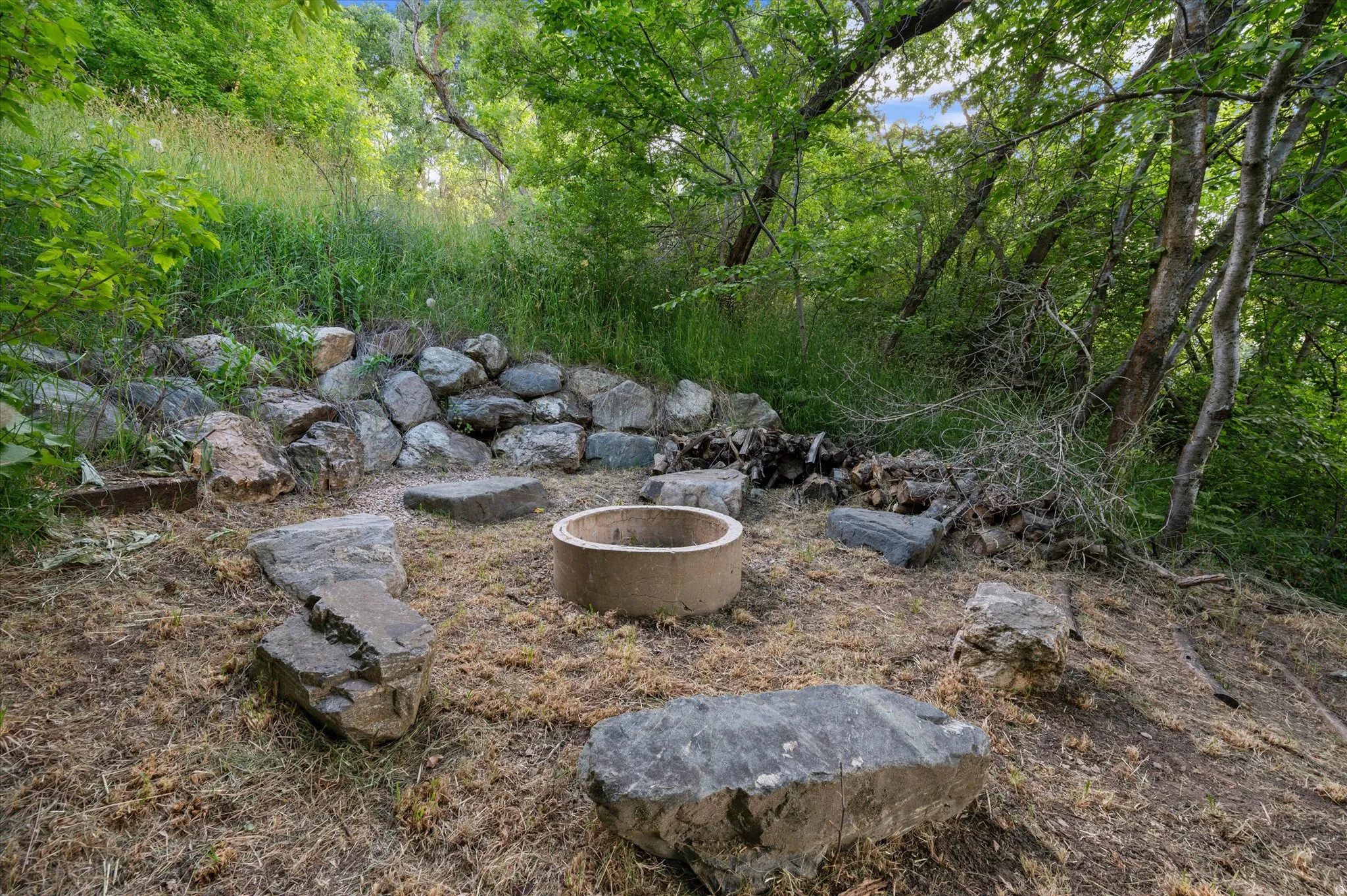 Outdoor fire pit area featuring a concrete fire ring, surrounding natural stone seating, and a rock retaining wall