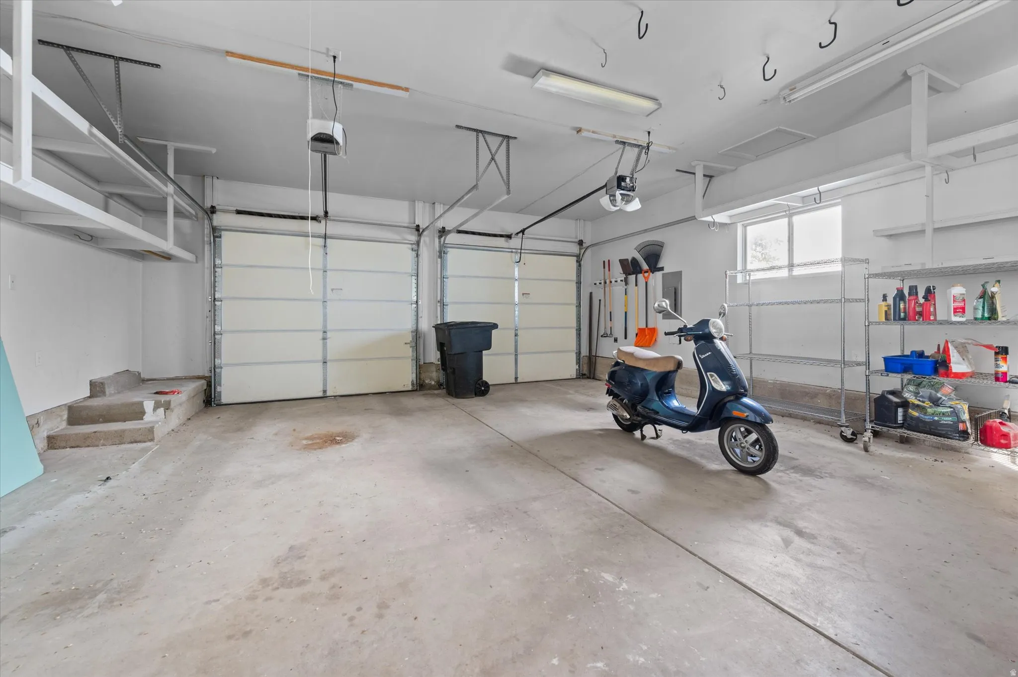 Spacious garage featuring two overhead doors, concrete flooring, overhead fluorescent lighting, and a rear window providing natural light
