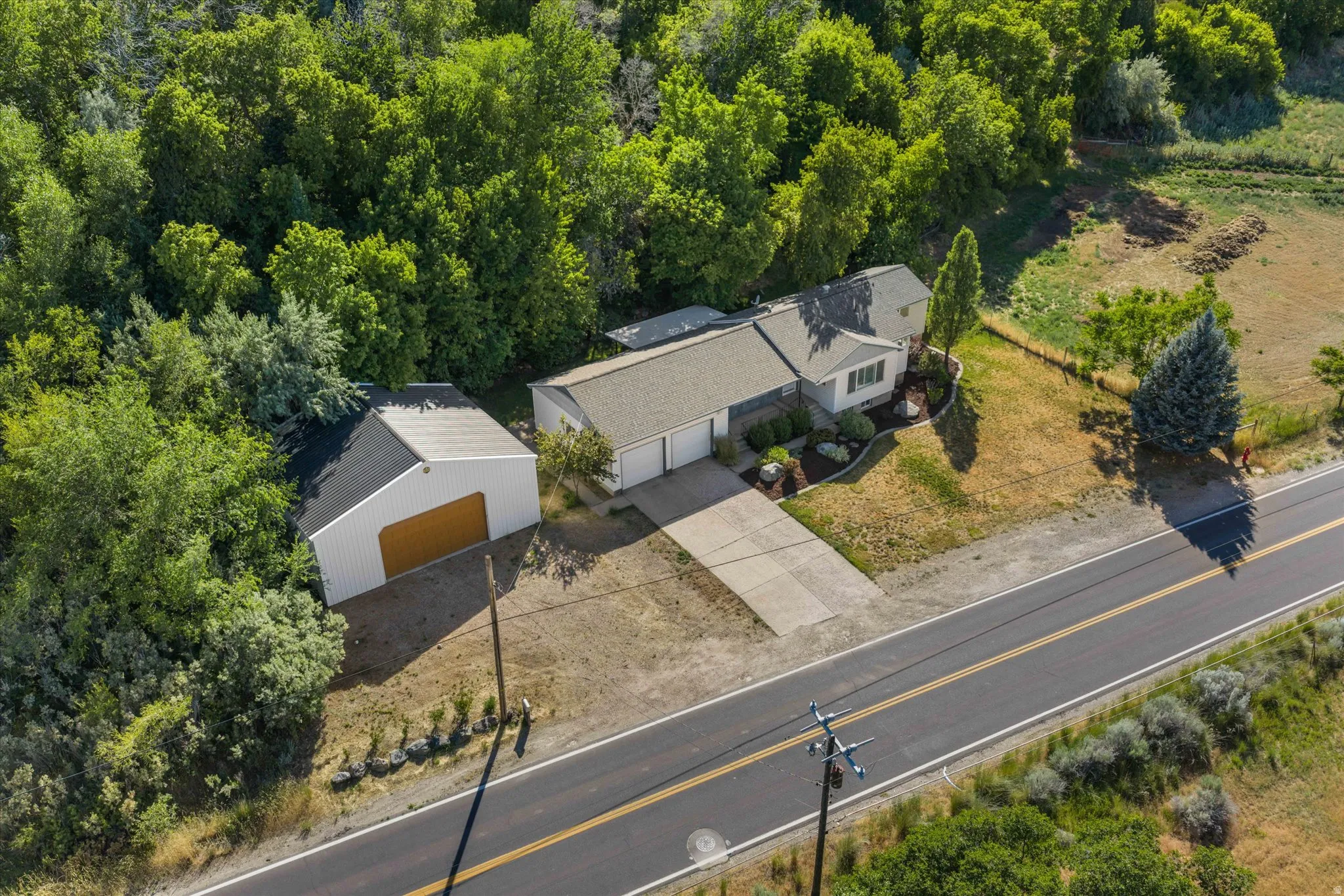 Ranch-style residence featuring an attached two-car garage, separate detached garage, paved driveway, mature landscaping, and surrounding wooded areas