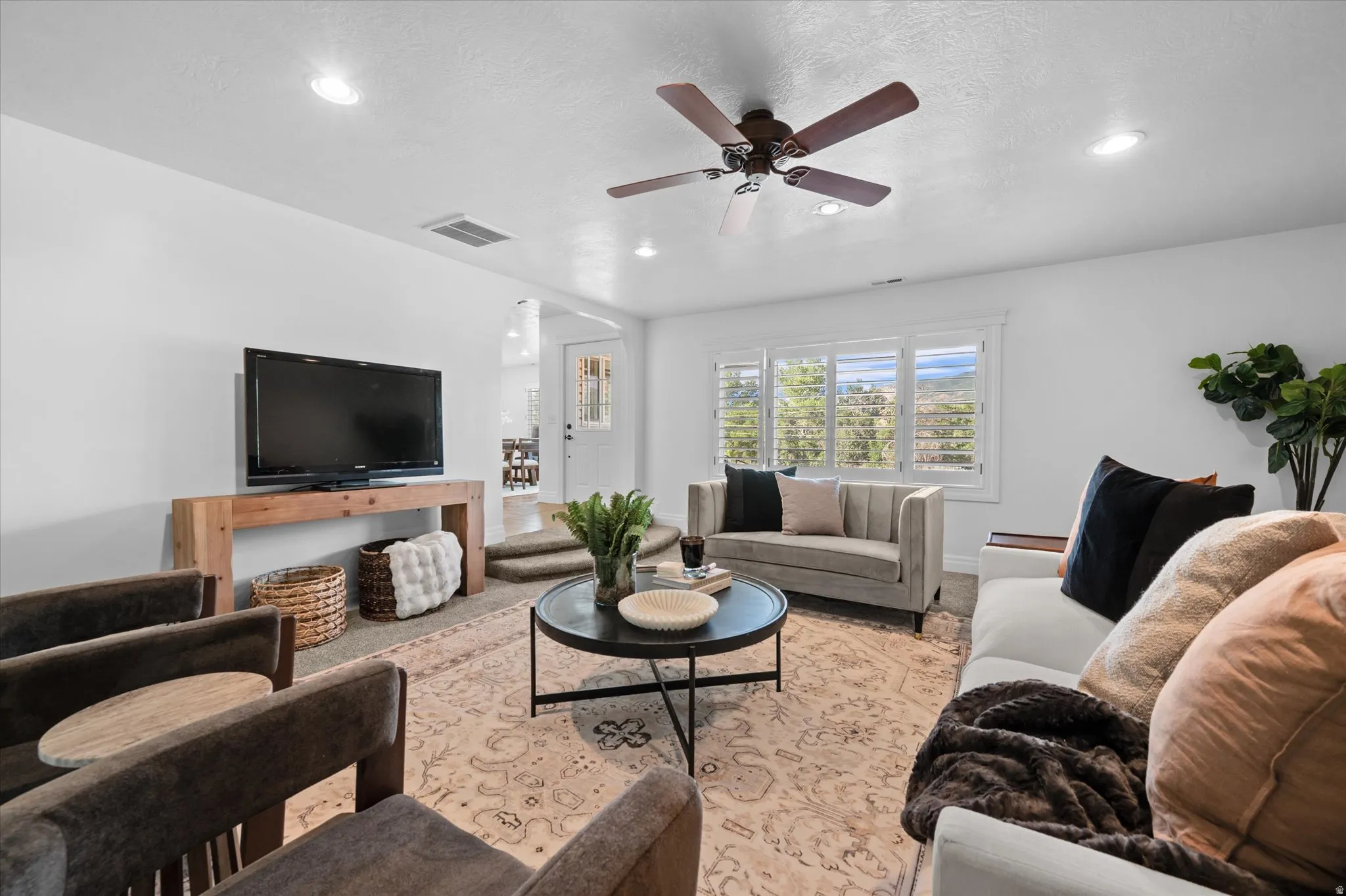Bright living area featuring white walls, recessed lighting, and a dark-toned ceiling fan