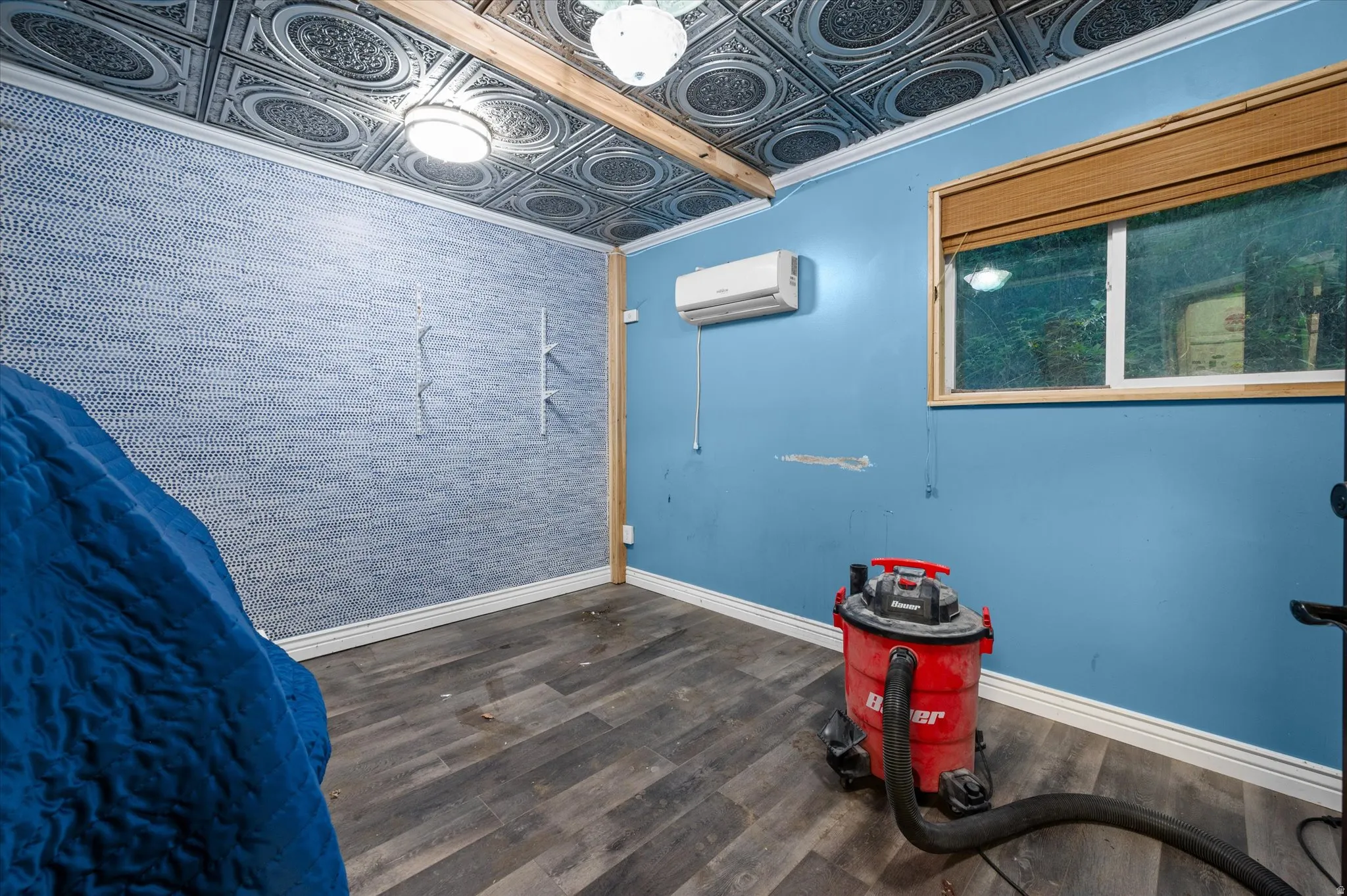 Room featuring wood-finish flooring, a textured accent wall, and a window with wood trim