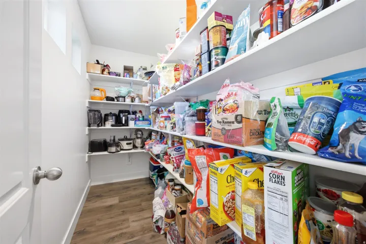 Walk-in pantry featuring extensive white shelving, wood-finish flooring, and white walls