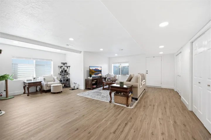 Spacious living area featuring light wood-finish flooring, recessed lighting, and bright white walls