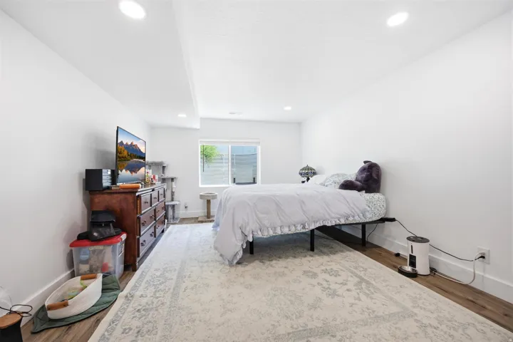 Bedroom featuring recessed lighting, a window with exterior visibility, wood-finish flooring, and white baseboards