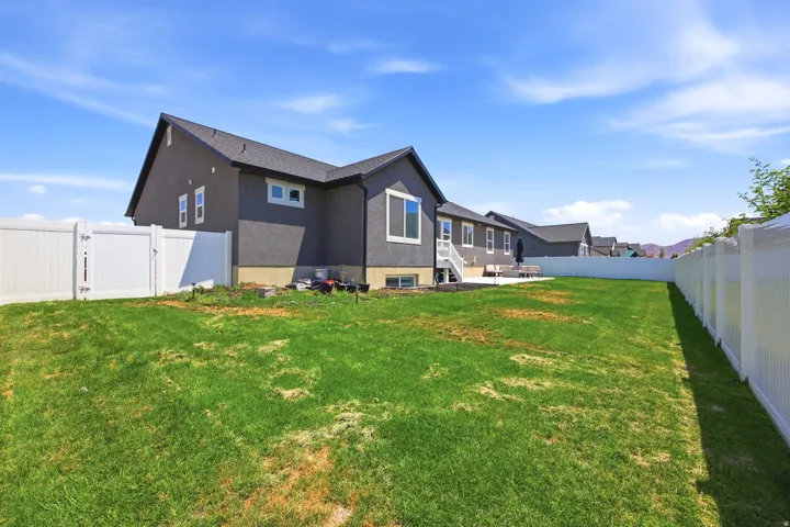 Expansive green lawn surrounds the property, featuring a full privacy fence and a rear patio