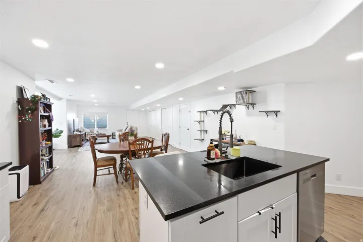 Spacious open-concept living area featuring a kitchen island with black countertop and integrated sink, recessed lighting, wood-finish flooring, and white walls