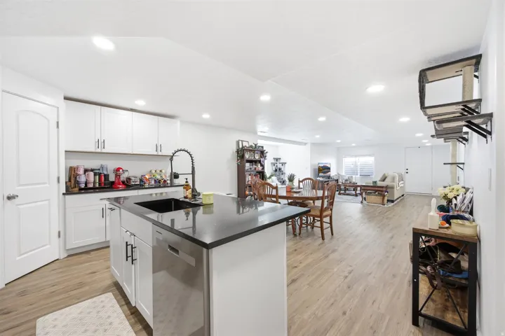 Open-concept living space featuring a central kitchen island with a dark sink and faucet, white cabinetry, dark countertops, and wood-finish flooring throughout