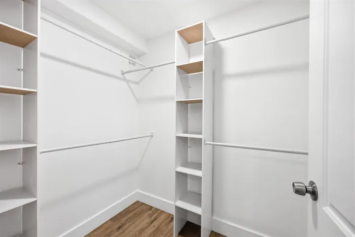Walk-in closet featuring built-in shelving, multiple hanging rods, white walls, white baseboards, and wood-finish flooring