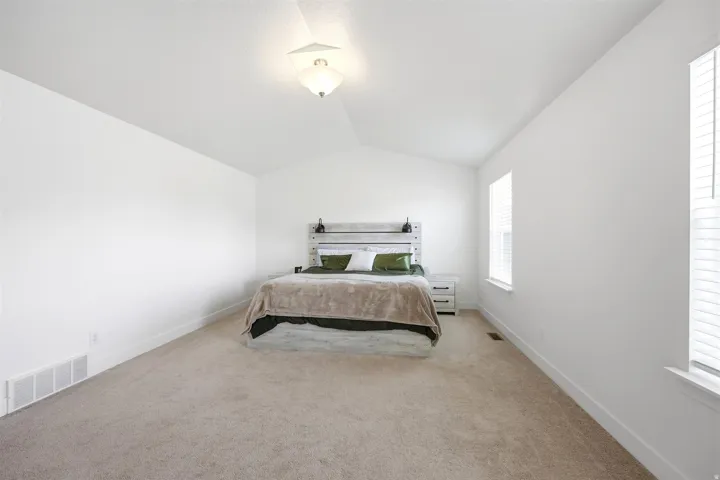 Spacious room featuring vaulted ceilings, light-toned carpeting, multiple windows with blinds, and white wall finishes