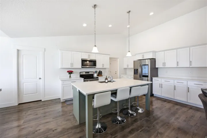 Spacious kitchen featuring an expansive island with seating, white shaker cabinetry, stainless steel appliances, and vaulted ceilings with recessed lighting