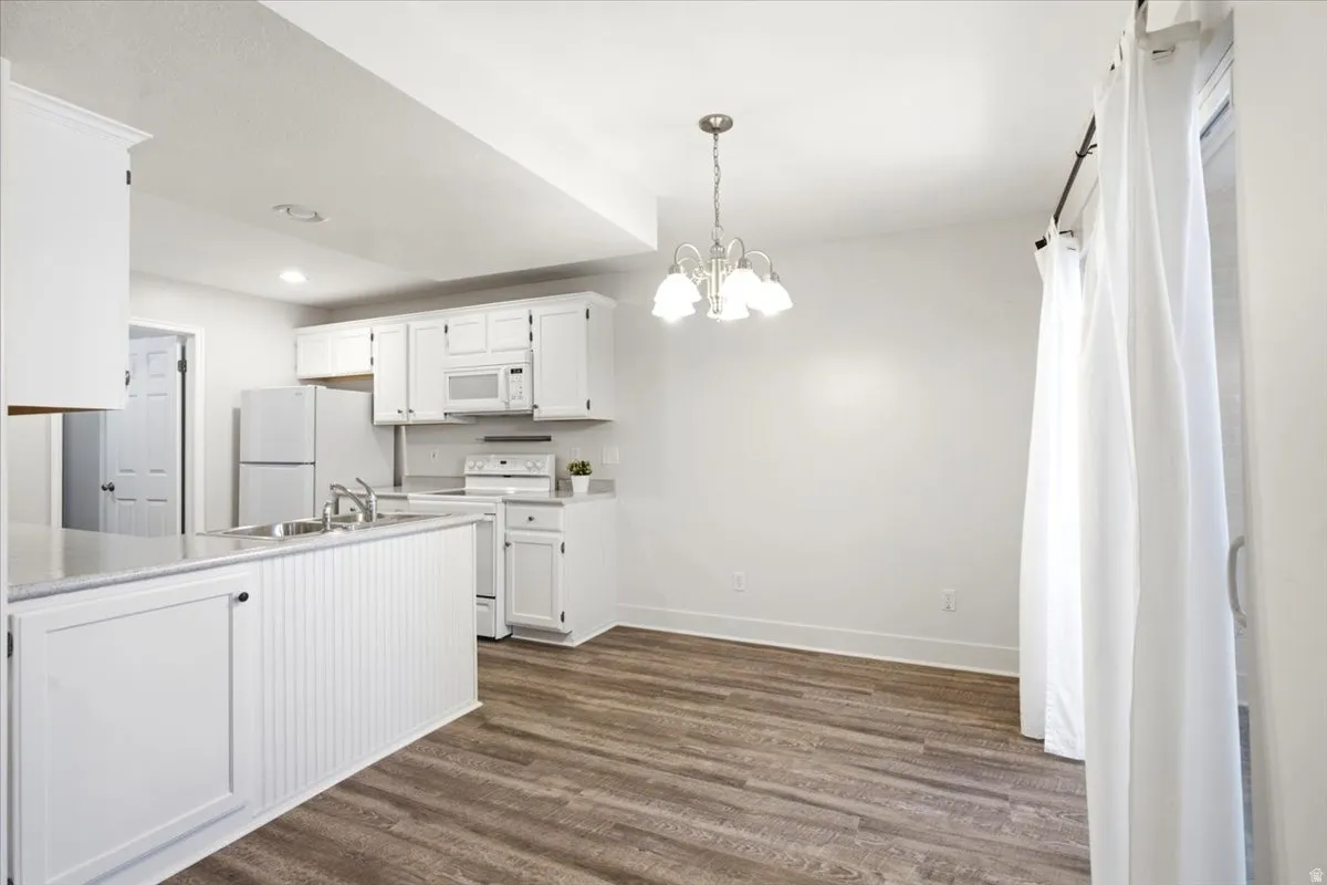 Open-concept kitchen and dining area featuring a white appliance package, white cabinetry, wood-finish flooring, and a sliding glass door