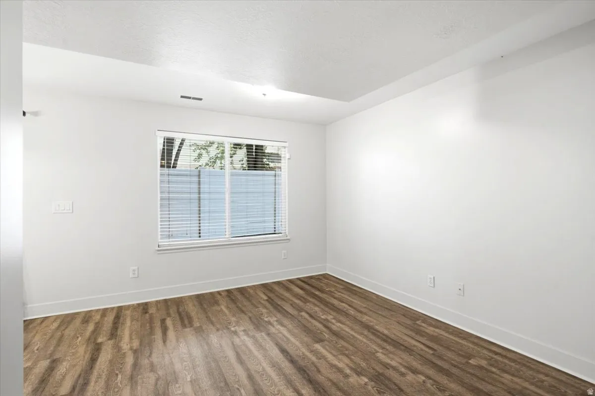 Spacious room featuring wood-finish flooring and a large window with horizontal blinds