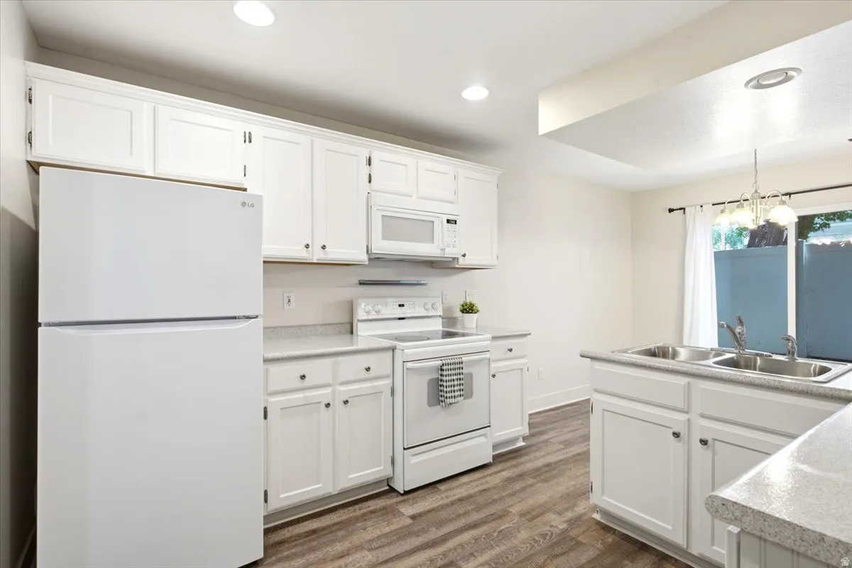 Kitchen featuring white cabinetry, wood-finish flooring, white appliances, recessed lighting, and a double basin sink