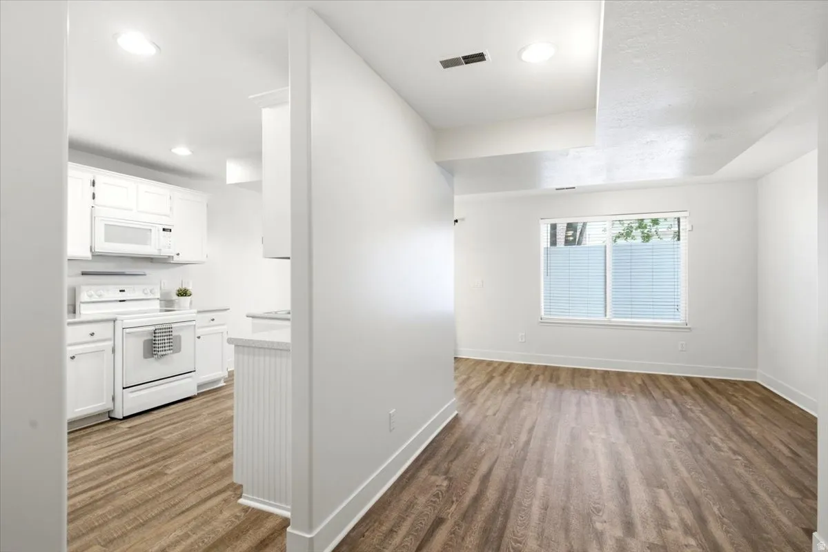 Bright open-concept living area featuring wood-finish flooring, white walls, and a large window with privacy blinds
