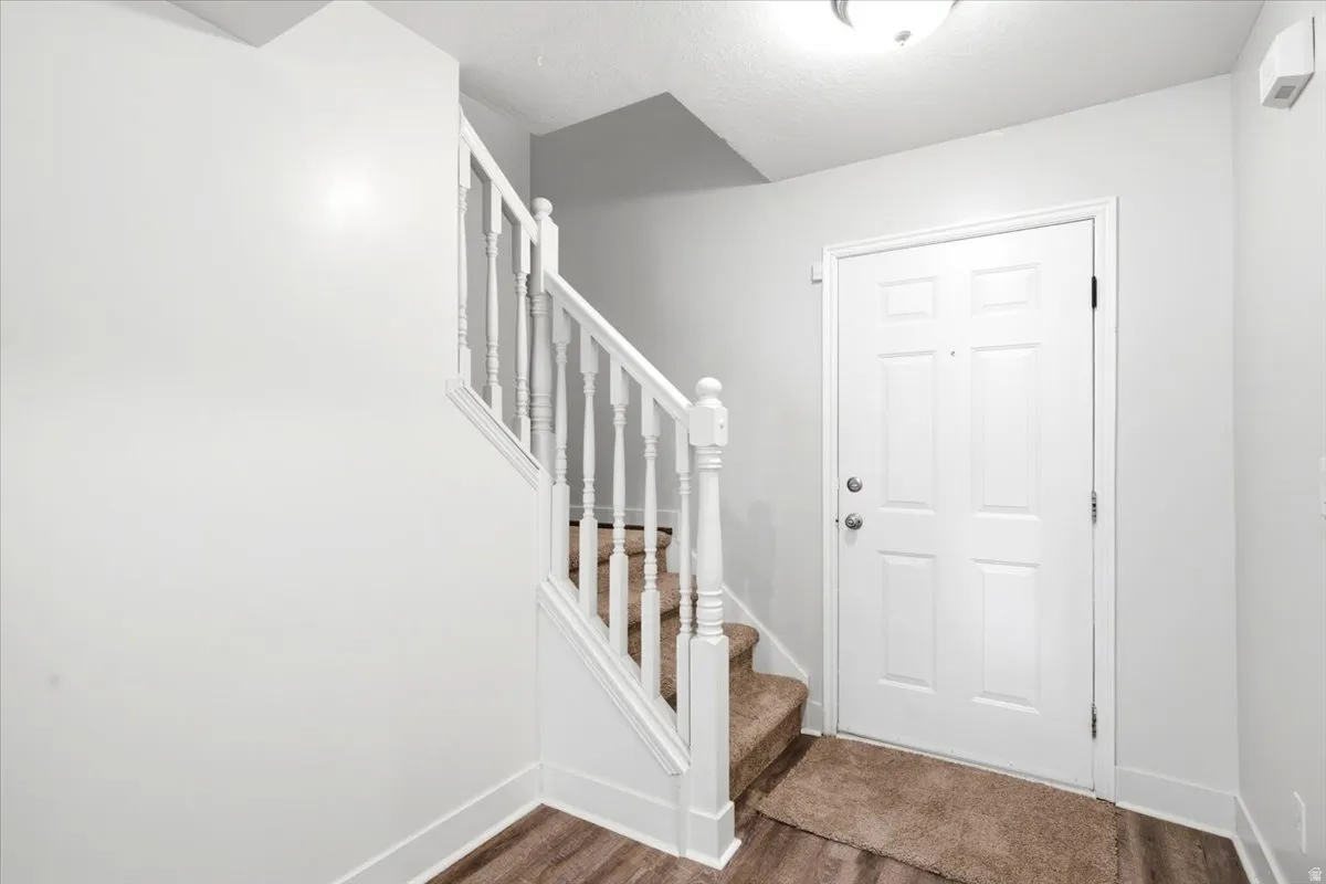 Entryway featuring a paneled door, wood-finish flooring, and a carpeted staircase with white balusters