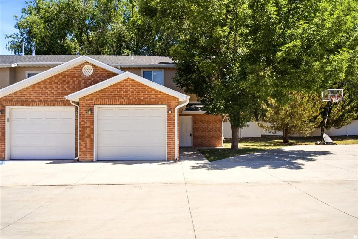Brick exterior featuring two white garage doors, a concrete driveway, and mature landscaping