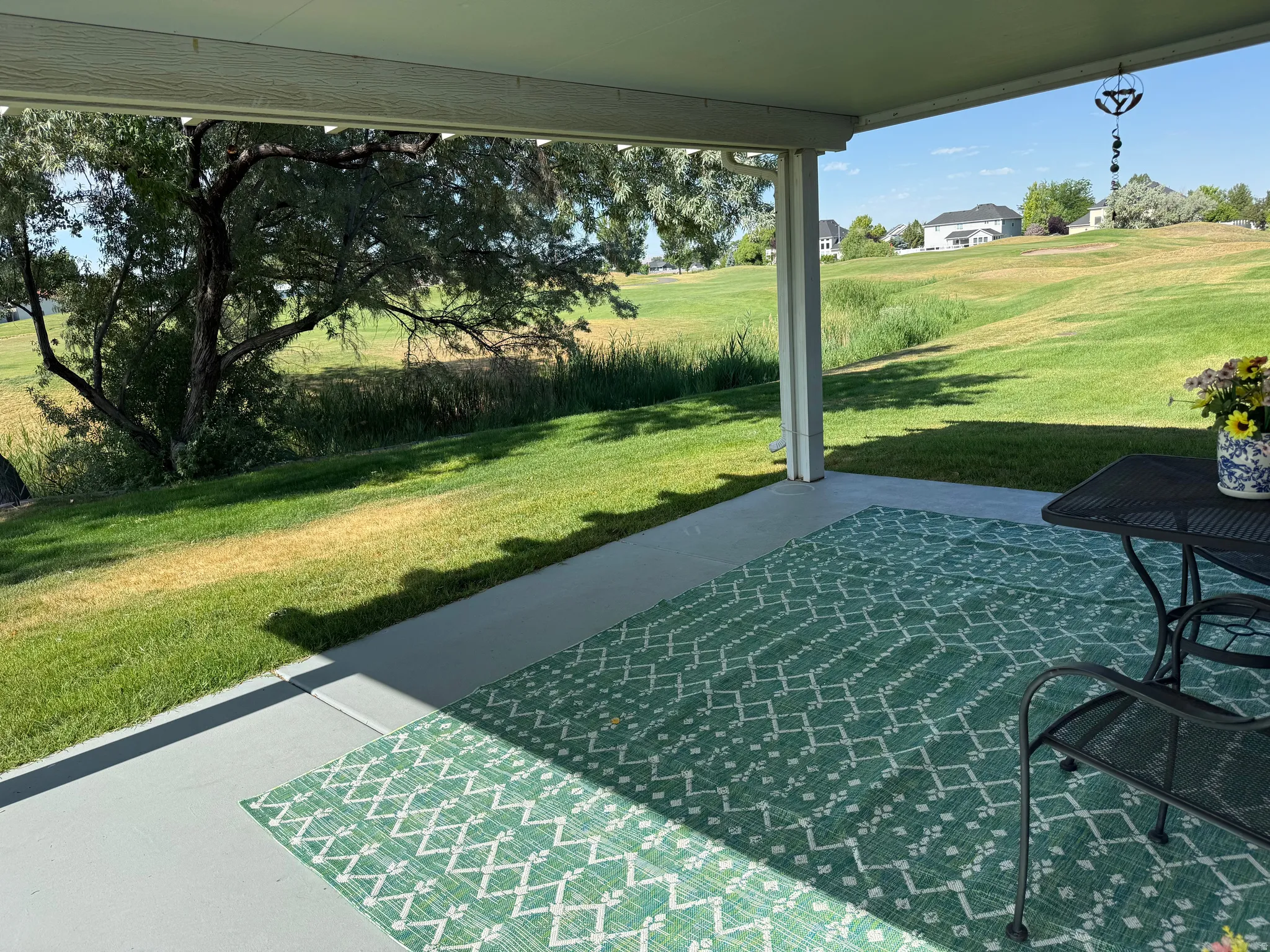Covered patio with concrete flooring overlooking a manicured lawn and mature trees