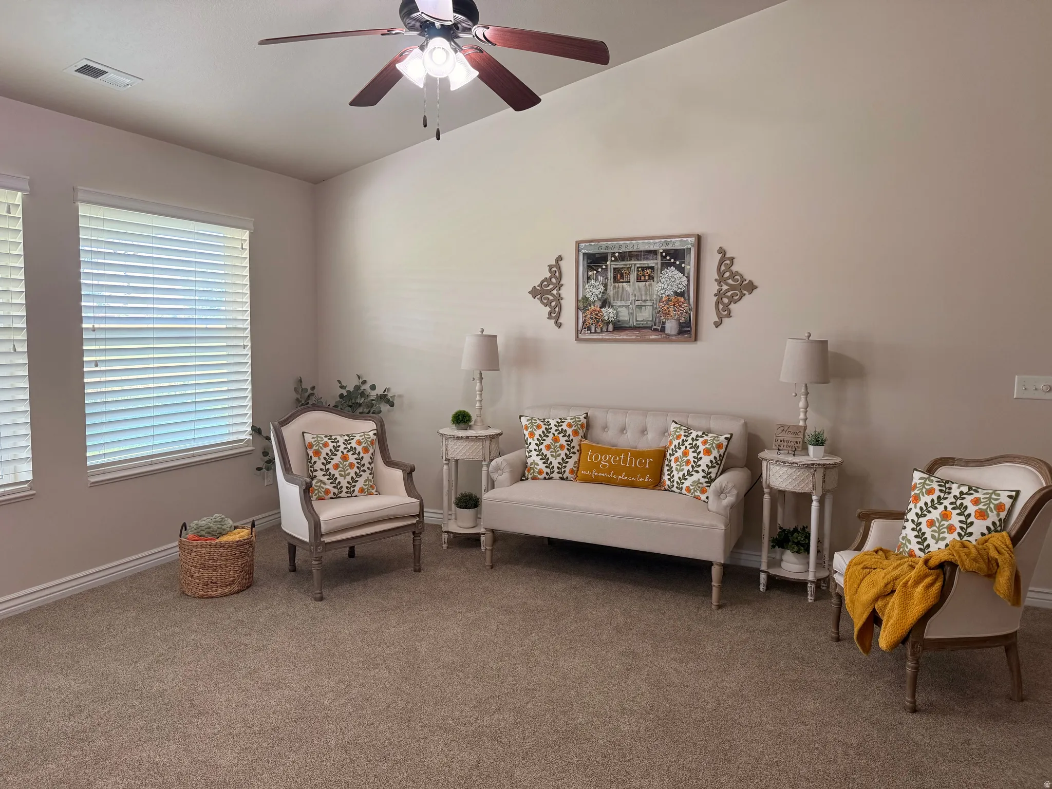 Bright living area featuring vaulted ceilings, a ceiling fan with integrated lighting, two large windows with blinds, and neutral carpeting