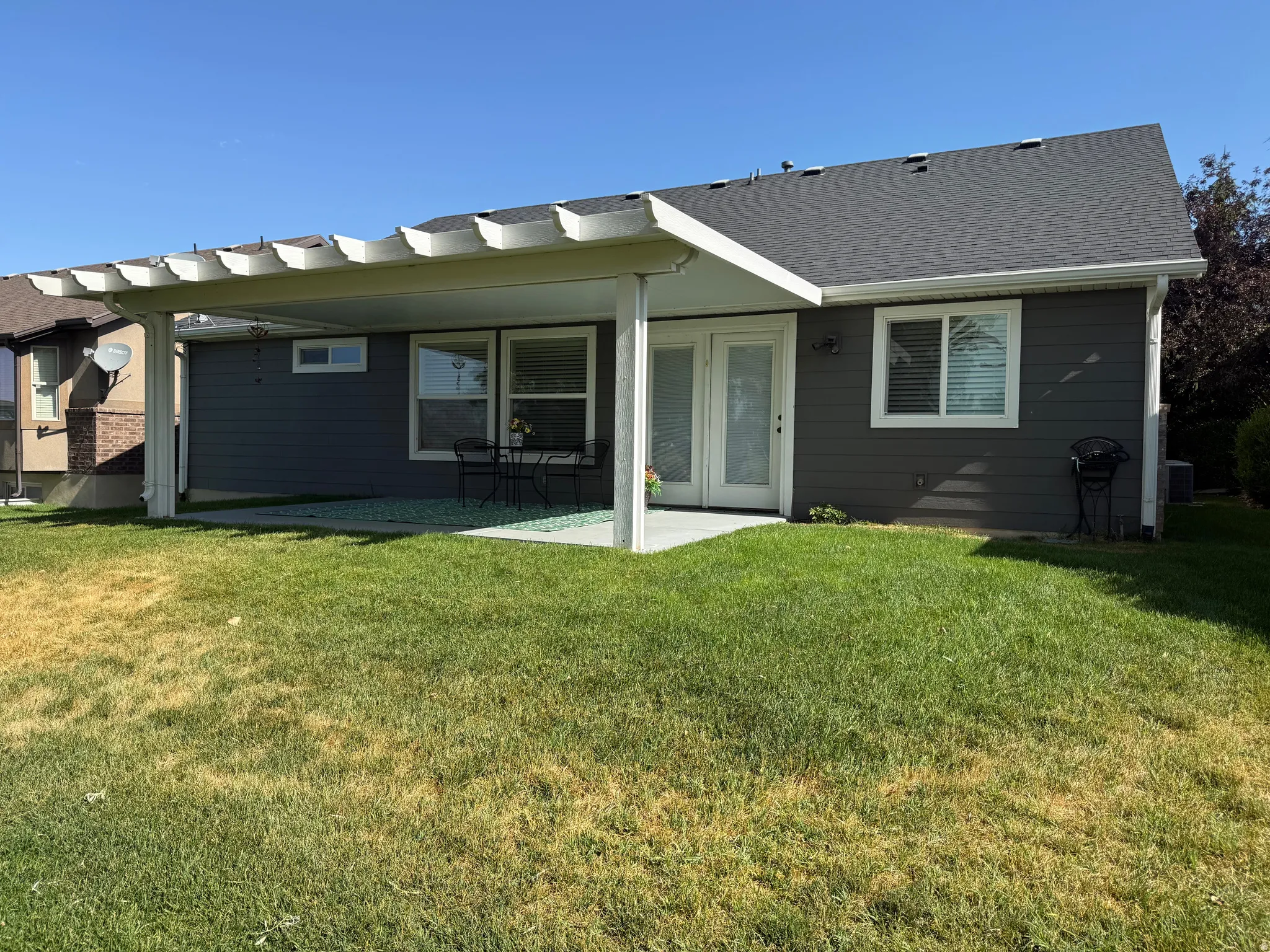 Expansive backyard featuring a covered concrete patio, a pergola extension, and a dual-pane glass door