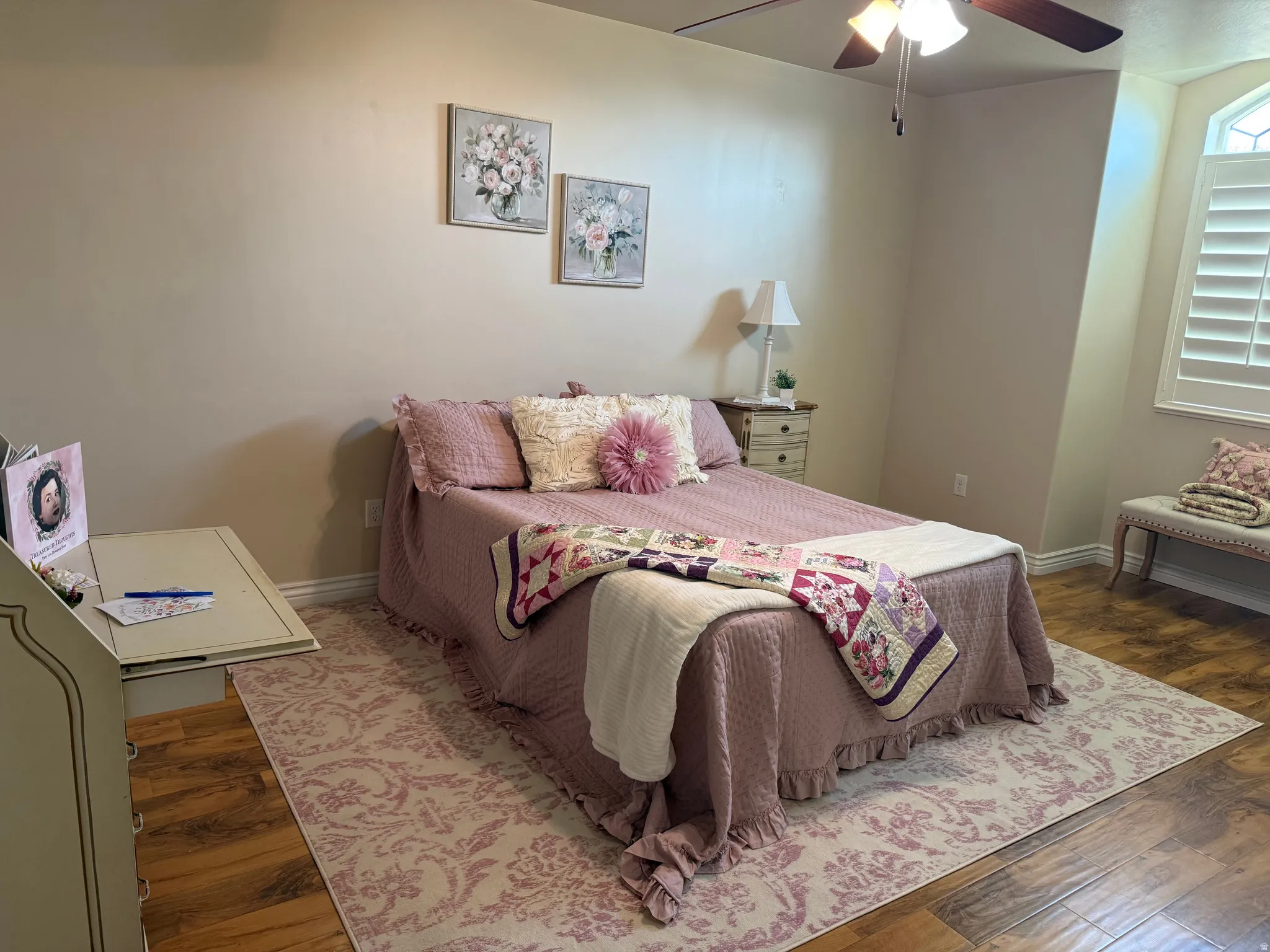 Bedroom featuring wood-finish flooring, a ceiling fan with integrated lighting, and a window with plantation shutters