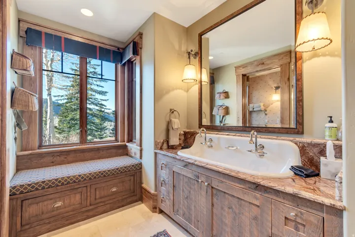 Spacious bathroom featuring a double vanity with a marble countertop, rustic wood-finish cabinetry, a large framed mirror, and two wall-mounted sconces