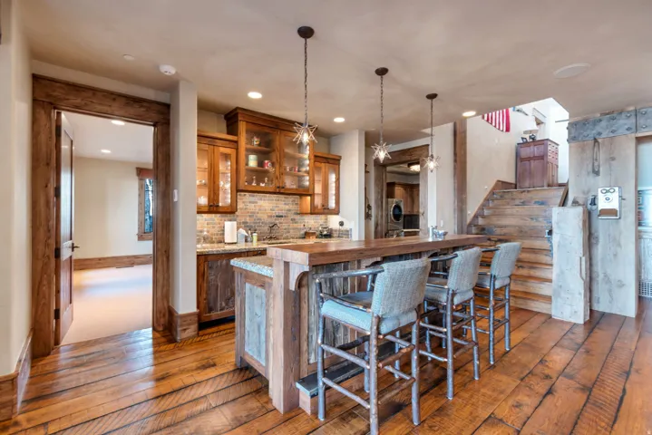 Rustic wood-finish flooring extending into a wet bar area featuring pendant lighting and built-in cabinetry with glass fronts